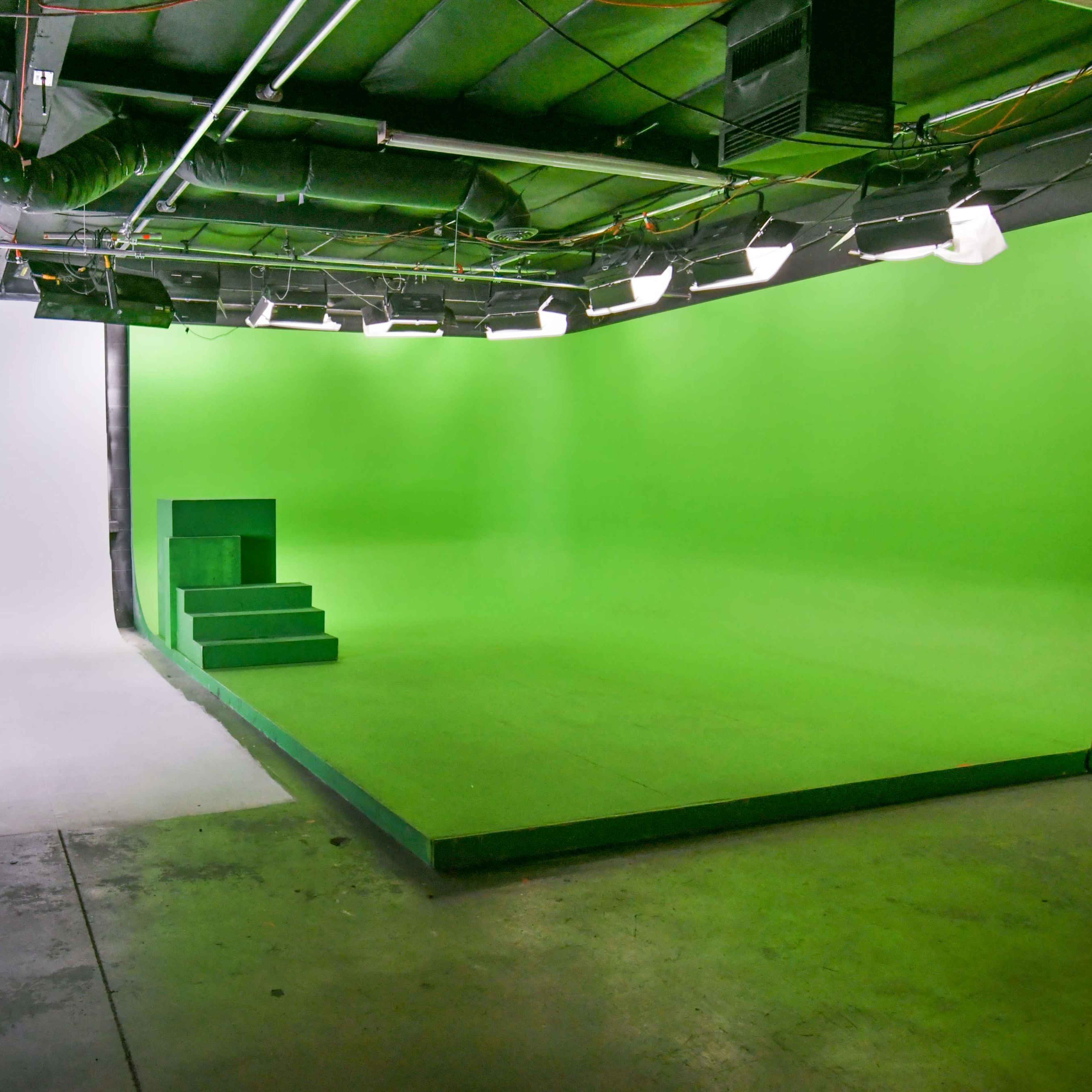 A studio space divided between a white backdrop on one side and a green screen with a raised platform on the other side.