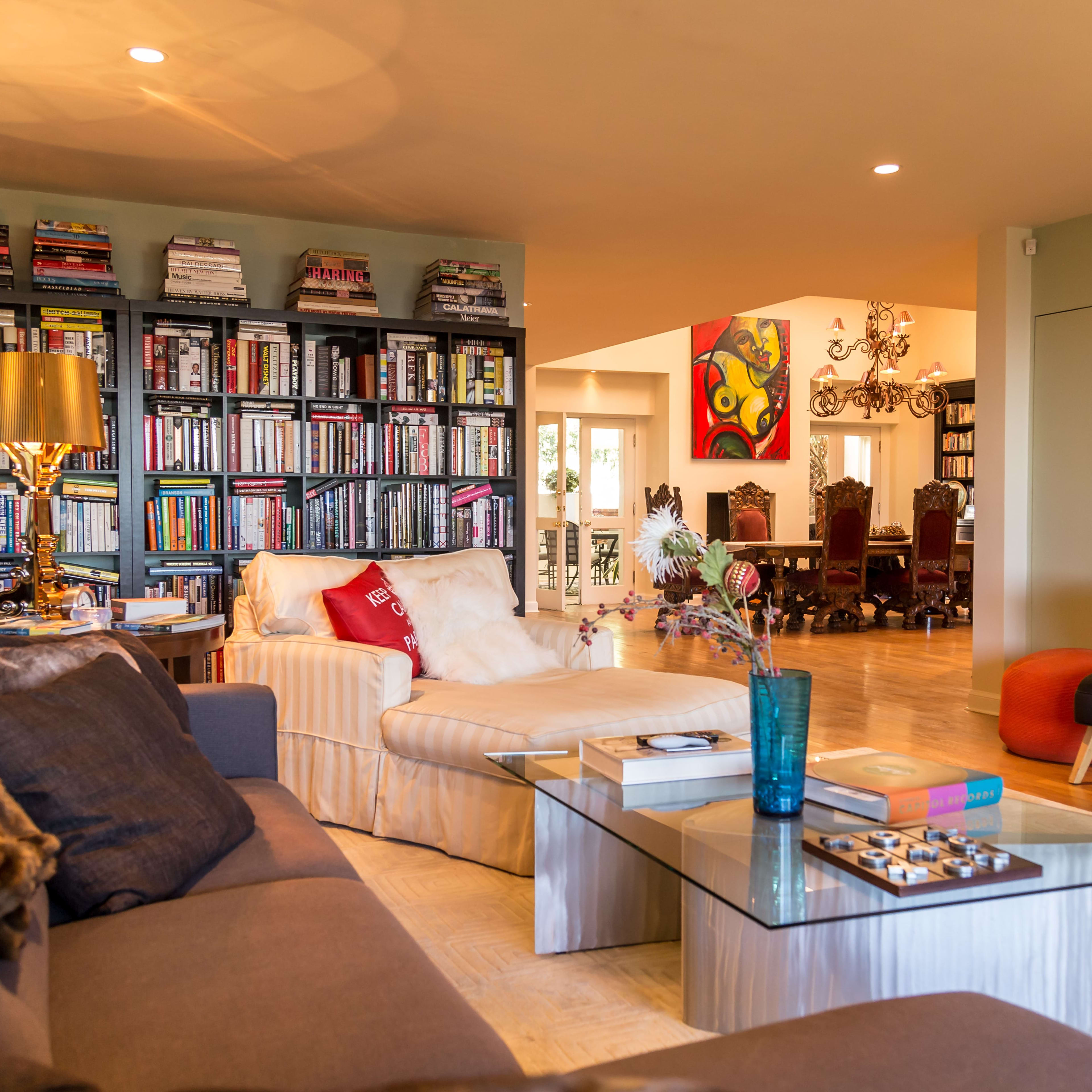 A stylish living room with a large bookshelf, a comfortable sofa, a glass coffee table, and a colorful artwork on the wall.