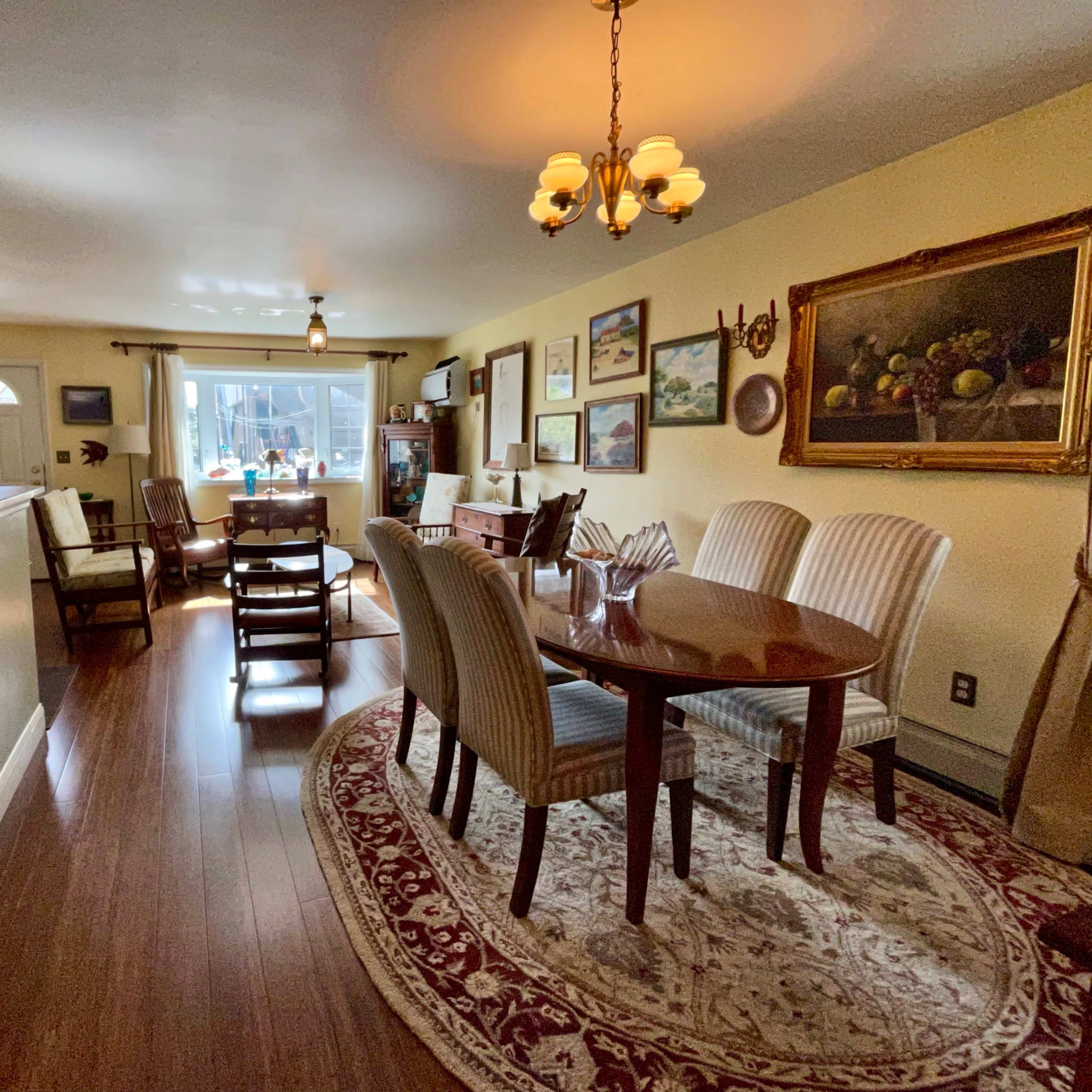 A dining area with a wooden table surrounded by upholstered chairs, a rug on the floor, and artwork on the walls.