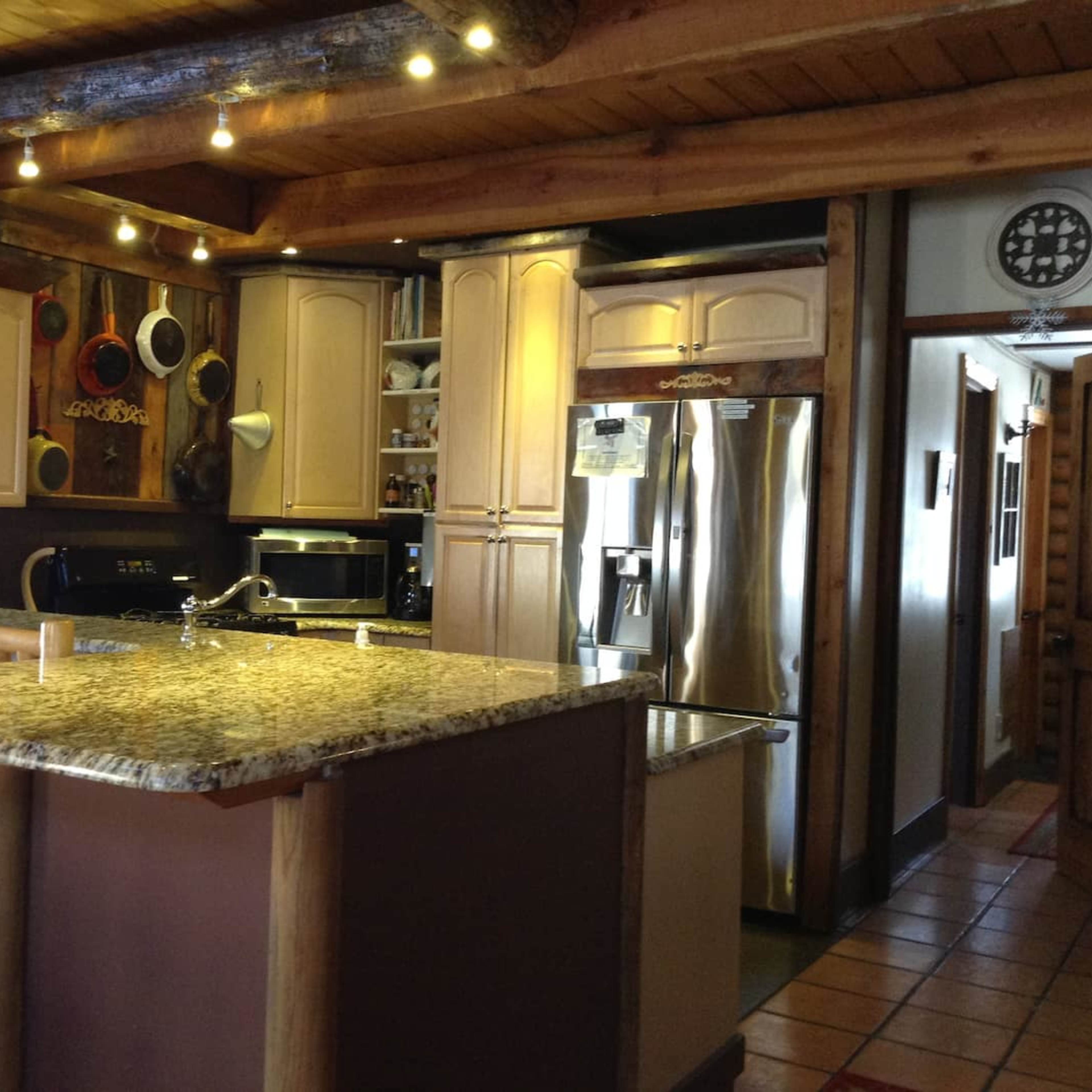 A kitchen with a central island topped with granite and wooden bar stools, surrounded by cabinetry and stainless steel appliances.
