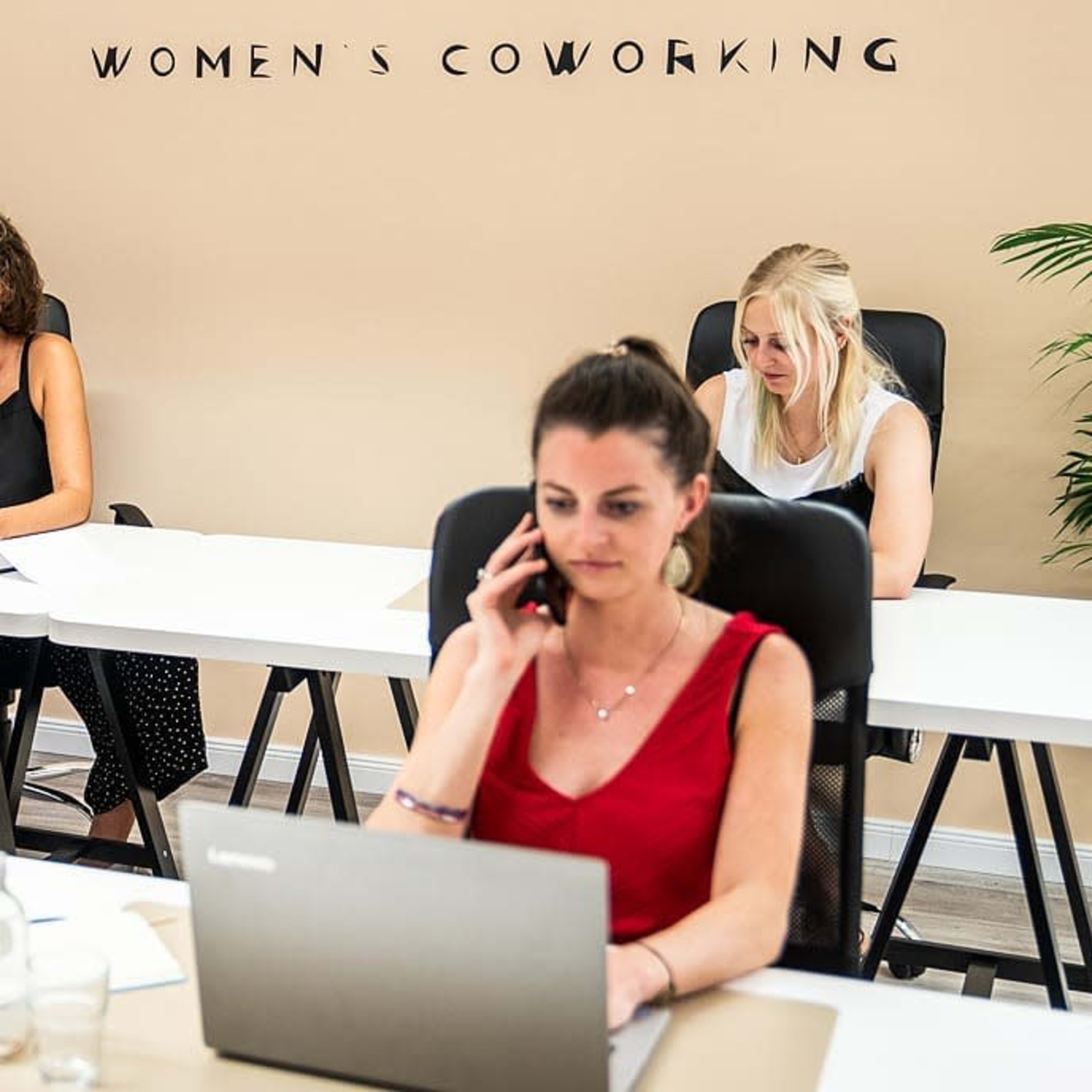A women's coworking space with three women working at desks, one on the phone and two focused on their laptops.