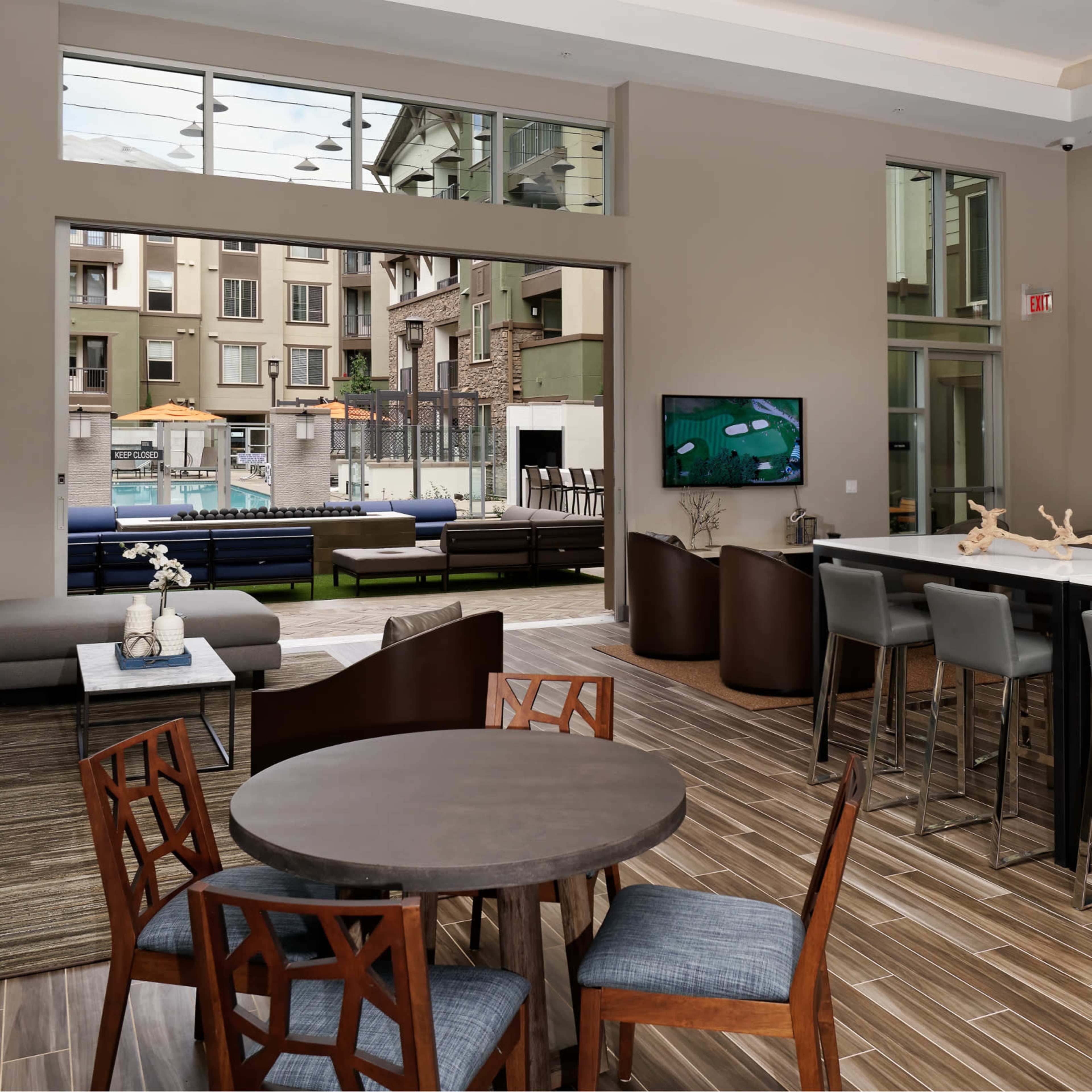 A contemporary lounge area with seating arrangements, a dining table, and a view of a pool through large windows.
