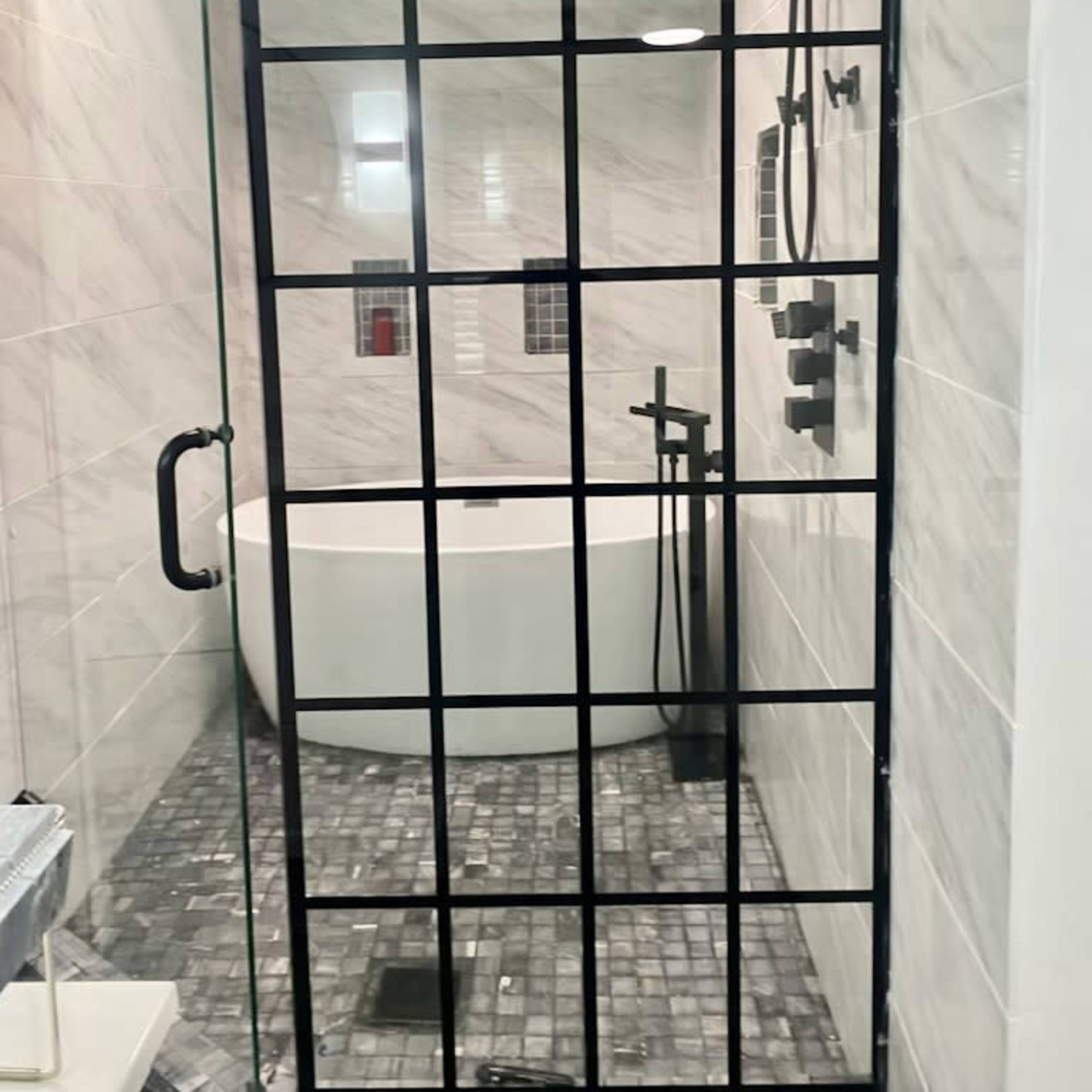 A modern bathroom featuring a glass shower enclosure with a black grid design, a freestanding bathtub, and a stone tile floor.