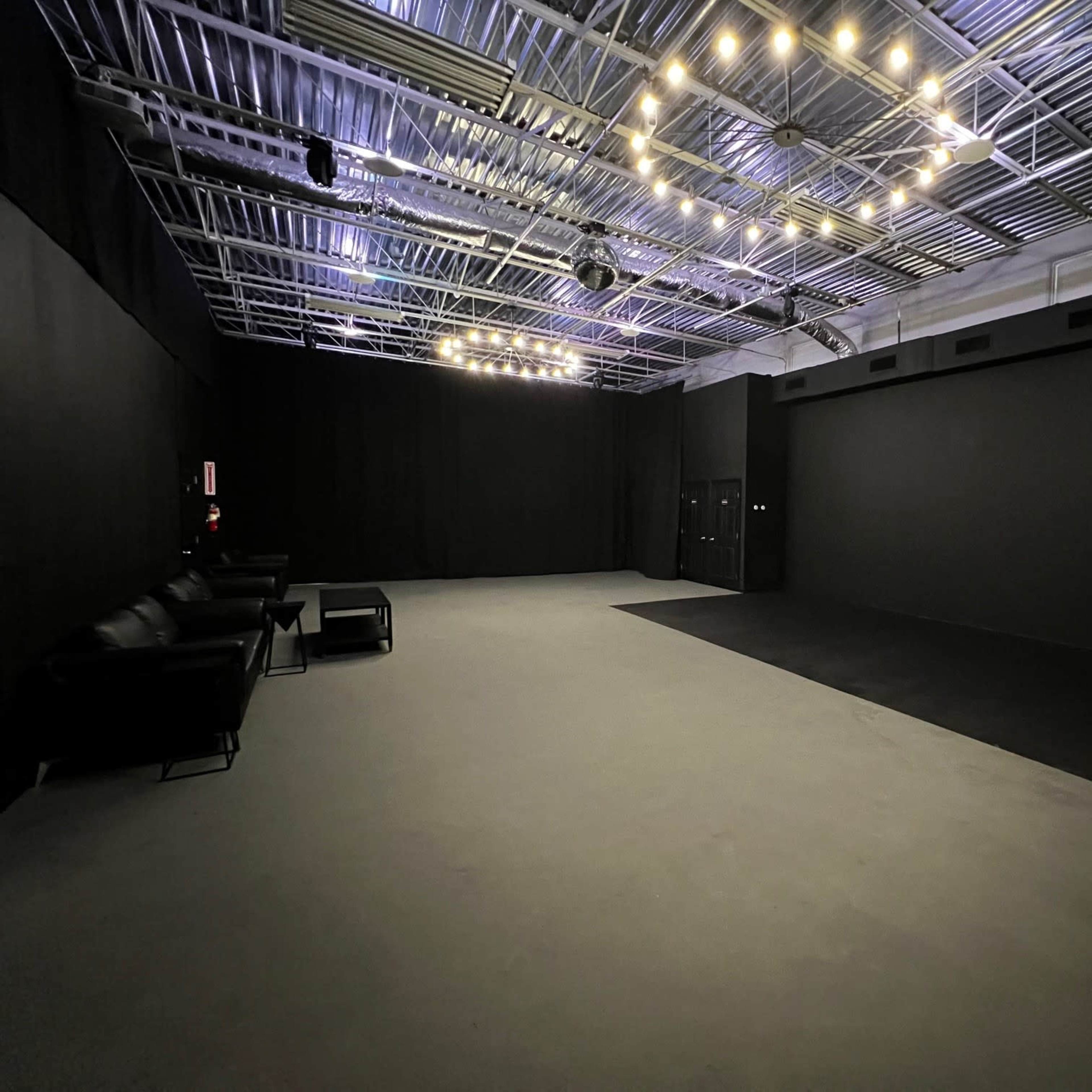 A large, empty studio space with a black floor and walls, illuminated by overhead lights.