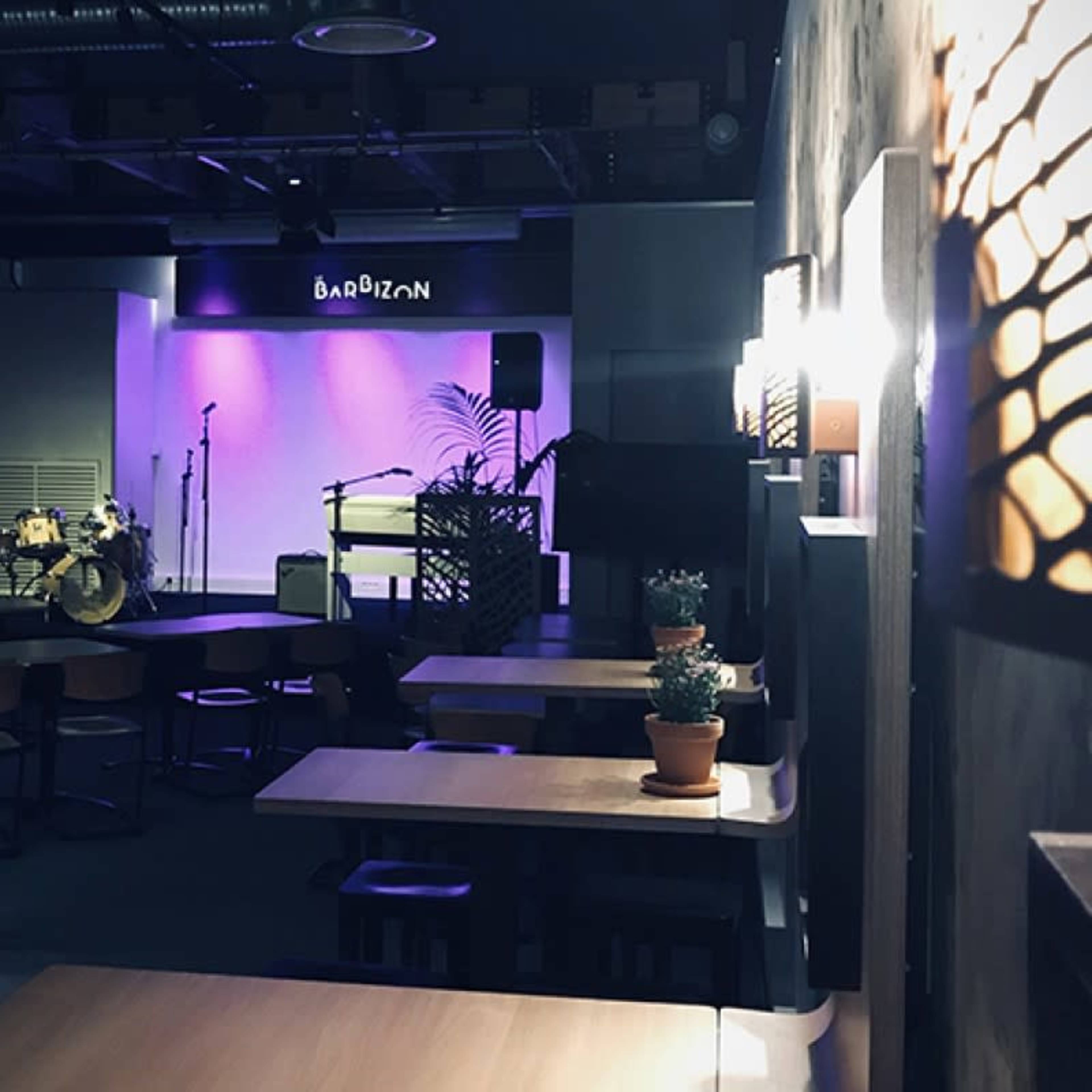 An empty bar and performance space with a stage featuring instruments and ambient purple lighting.