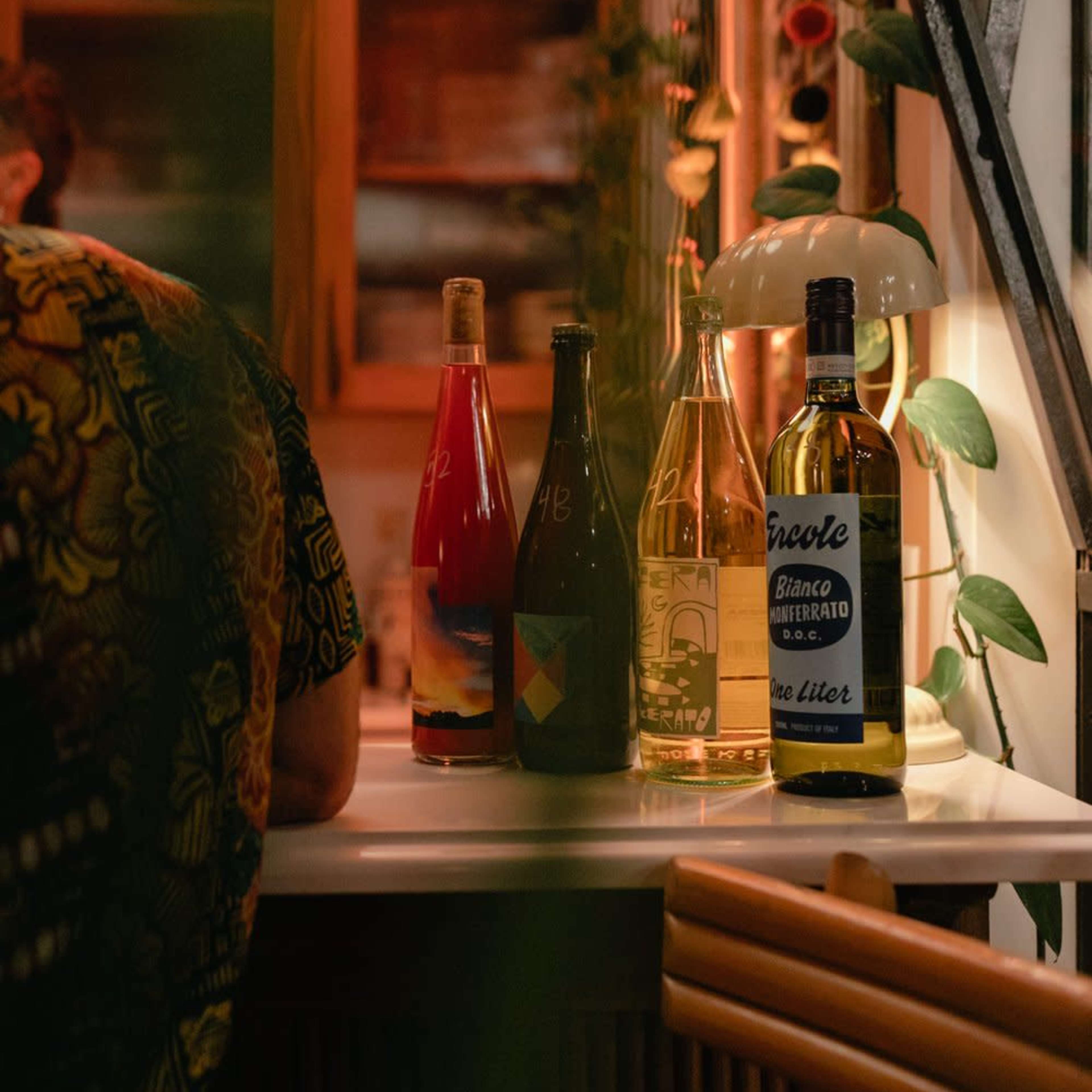 A person sits at a bar with four bottles of various beverages arranged on the counter in front of them.