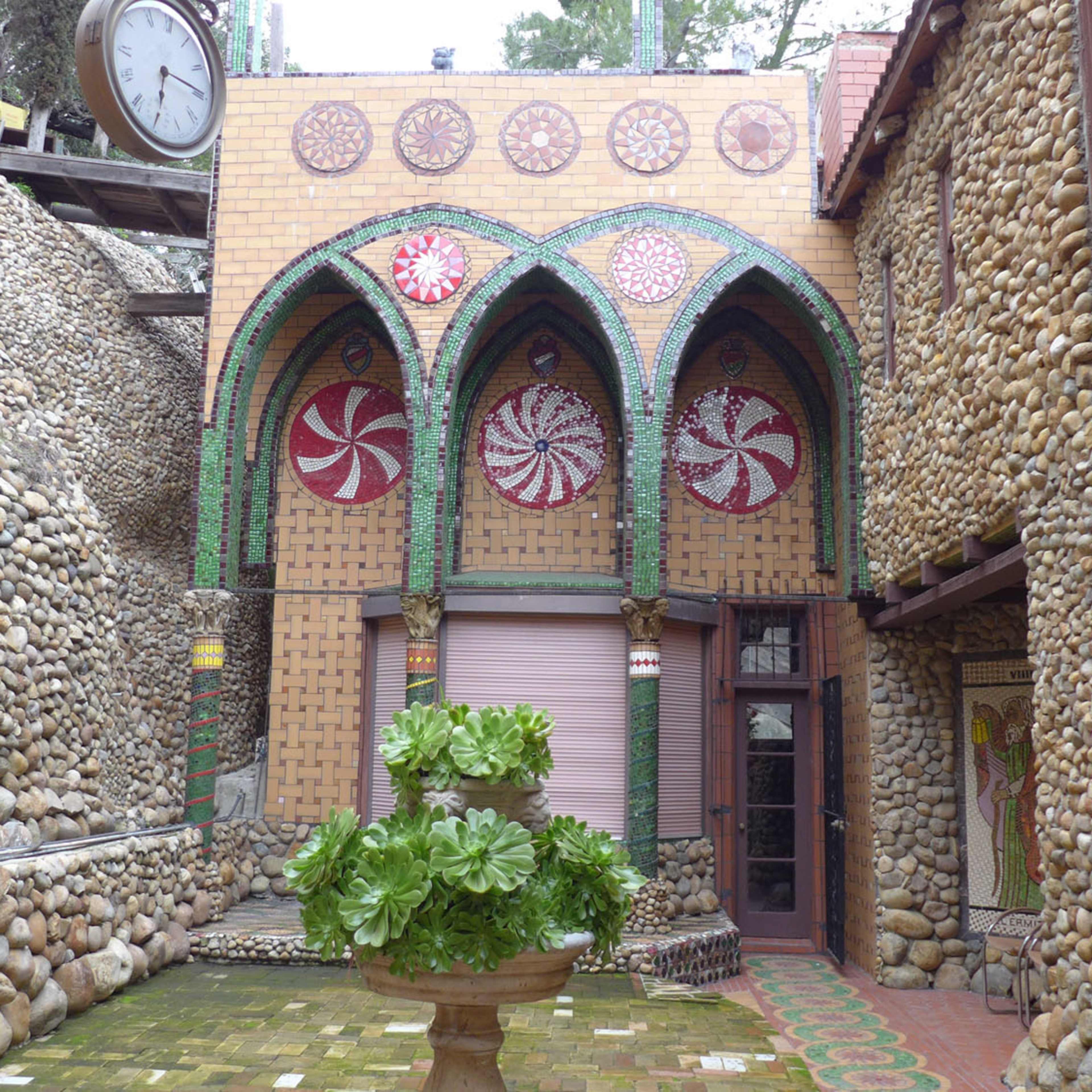 The scene features a courtyard with stone walls, decorative arches, and a central planter, surrounded by colorful tile patterns.
