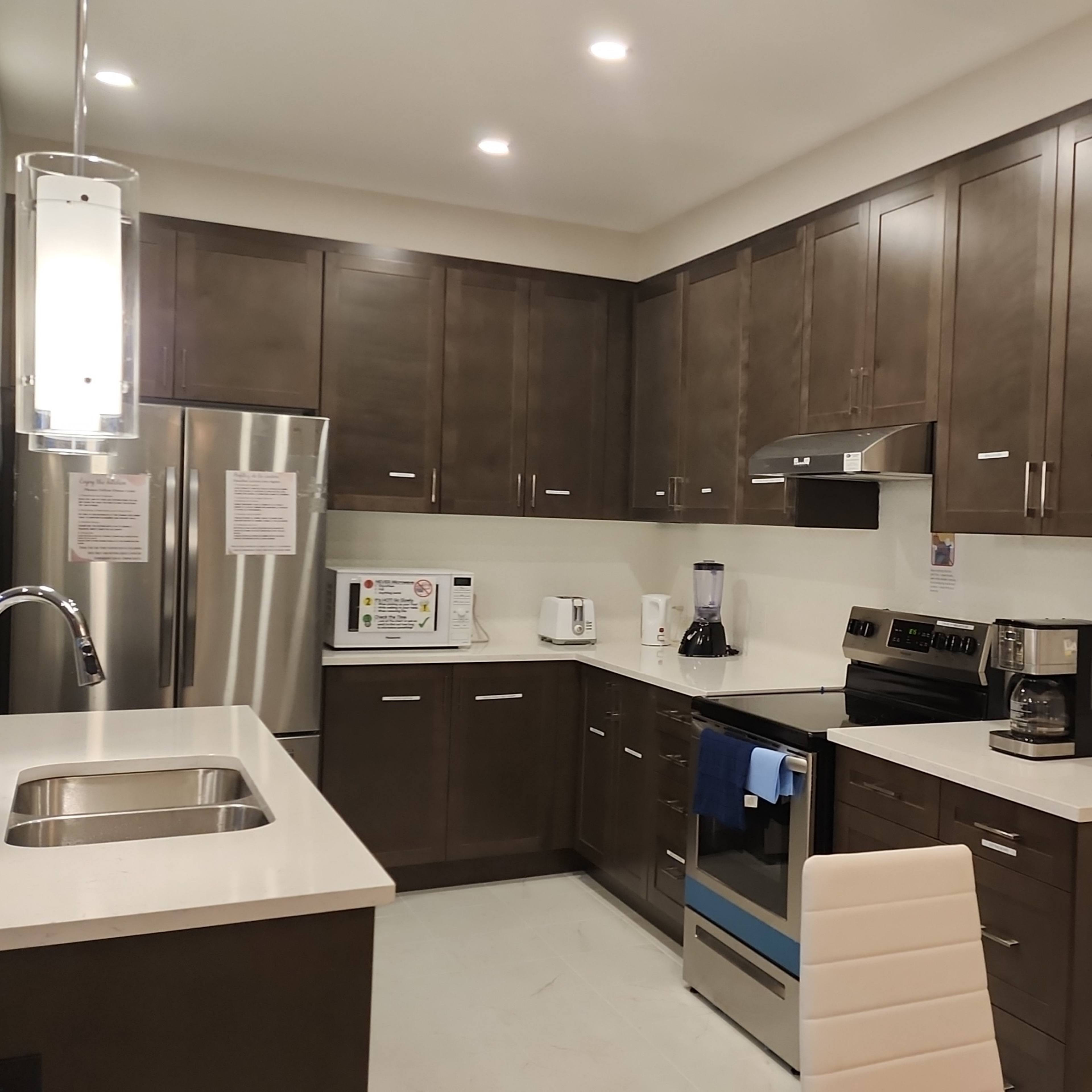 A modern kitchen with dark wood cabinetry, stainless steel appliances, and a white countertop.
