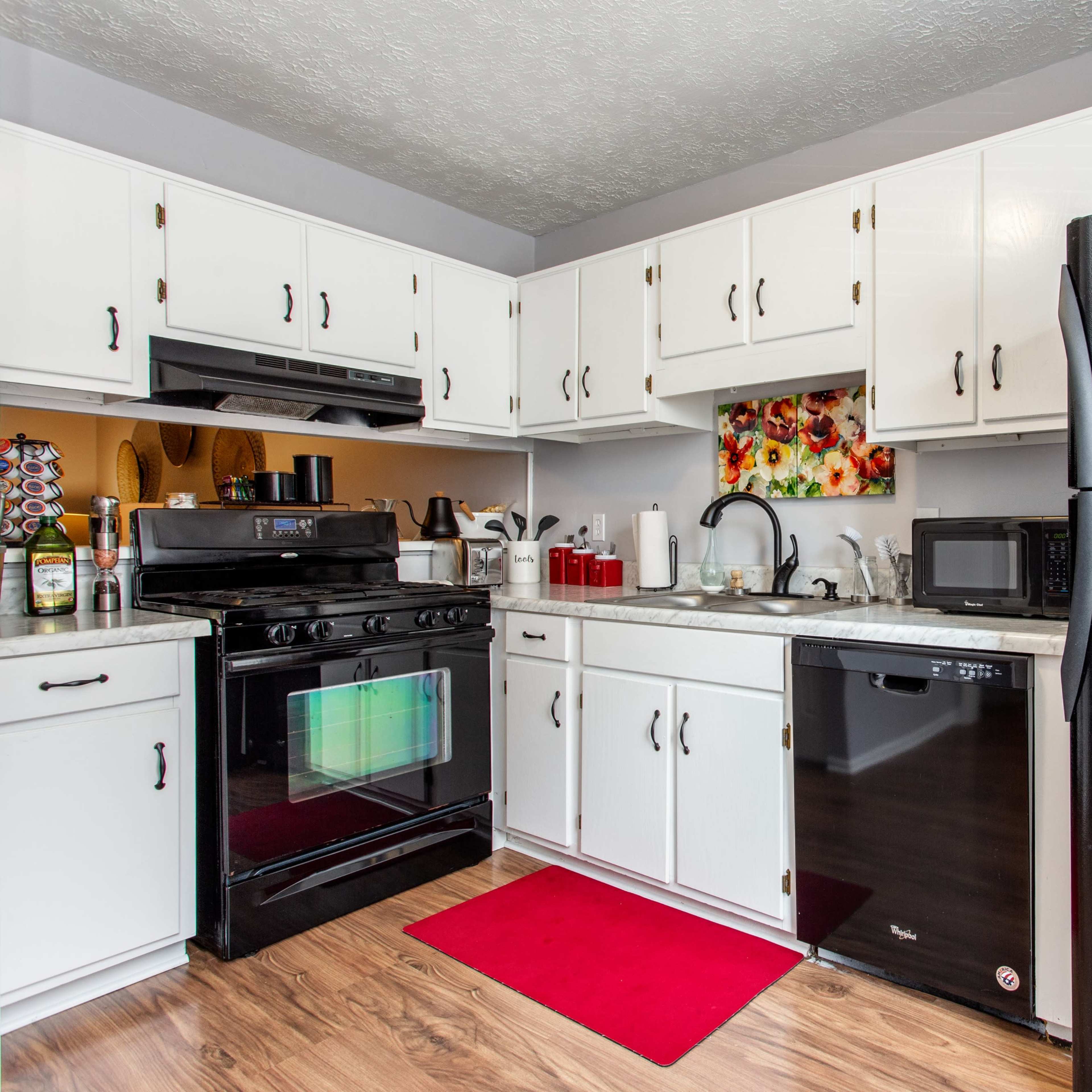 The kitchen features white cabinetry, black appliances, a red rug, and a floral wall decoration.