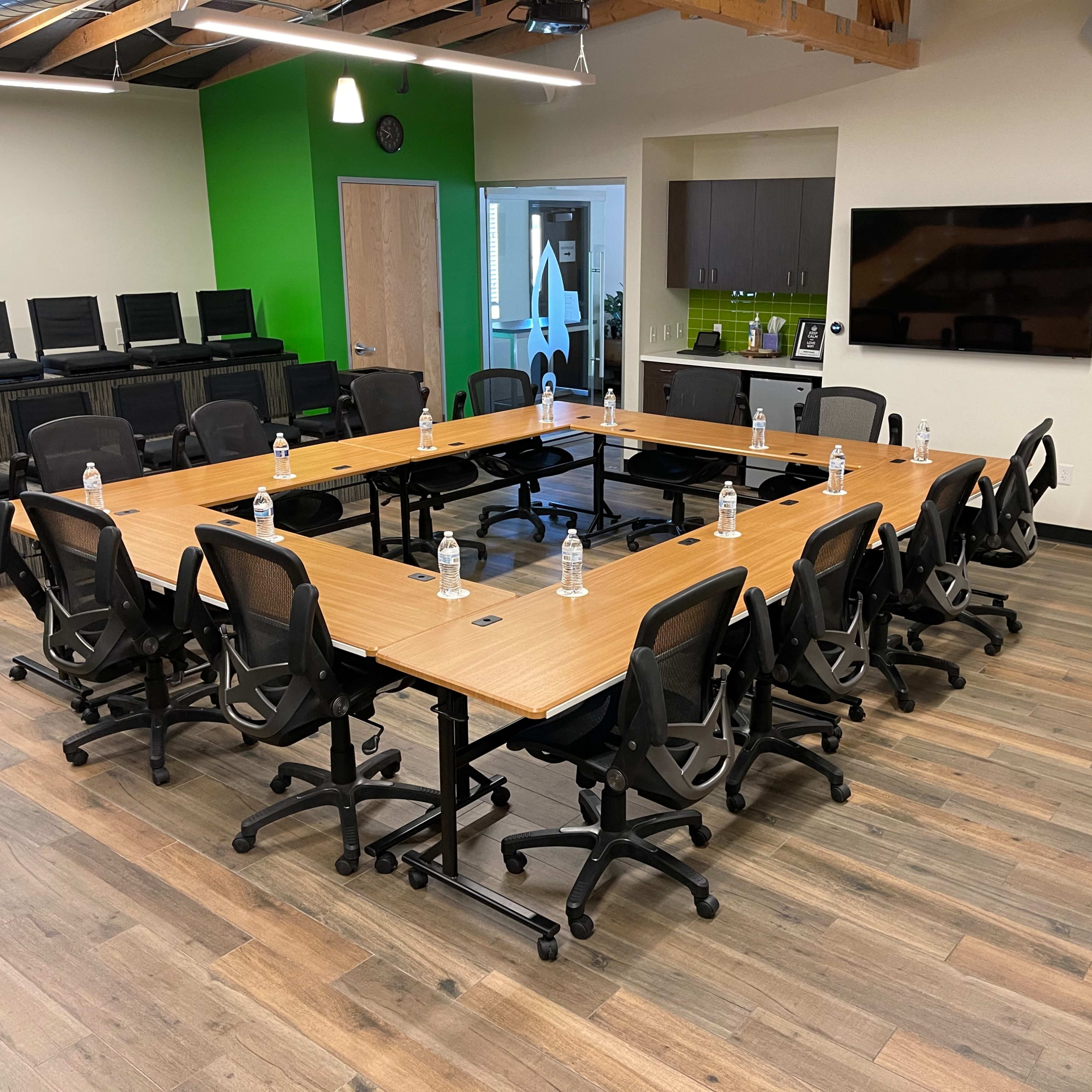 A conference room features a large rectangular table surrounded by ergonomic chairs, with water bottles placed at intervals on the table.