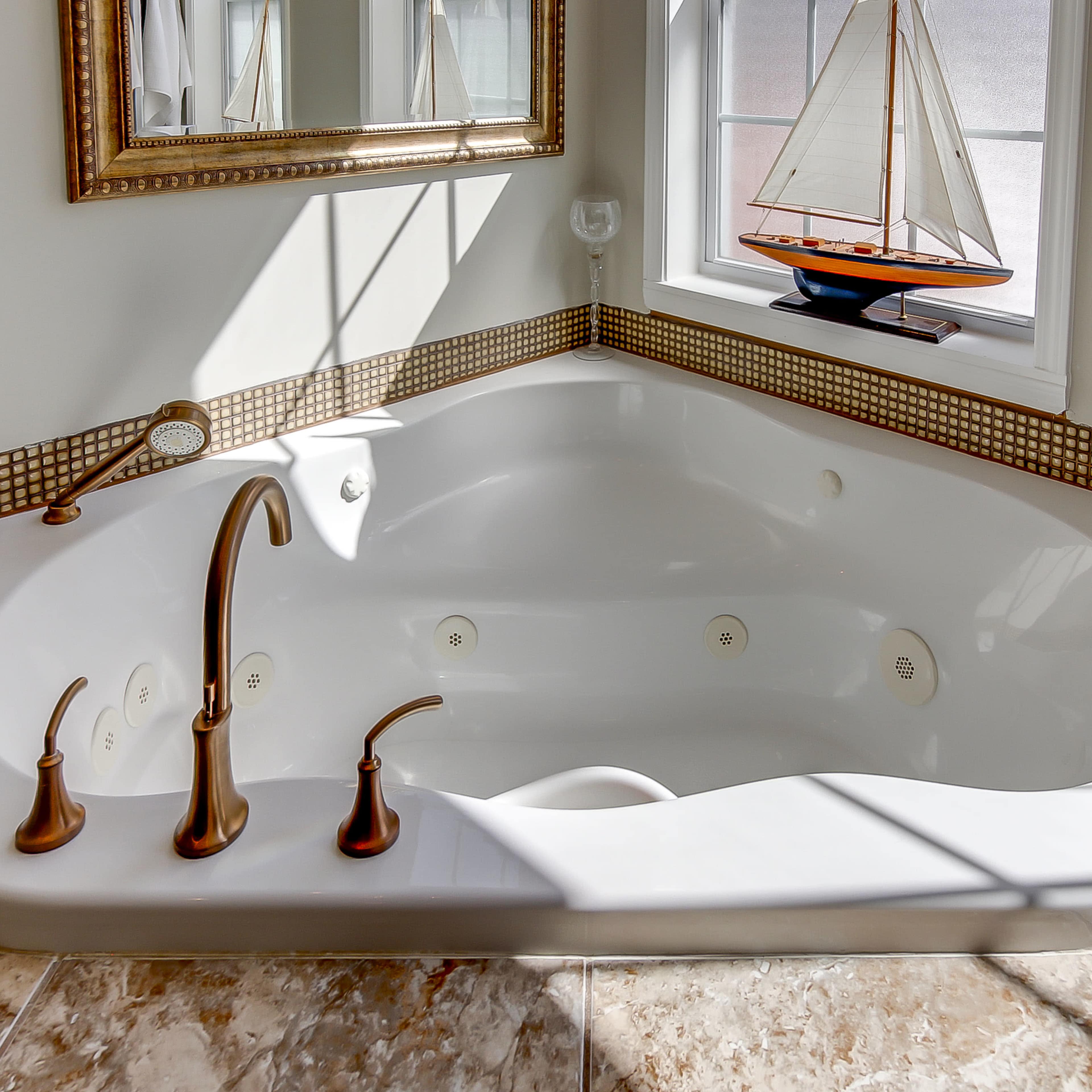 A corner jacuzzi tub with multiple faucets, set against a window displaying a small sailboat and framed by a mirror and decorative tile.