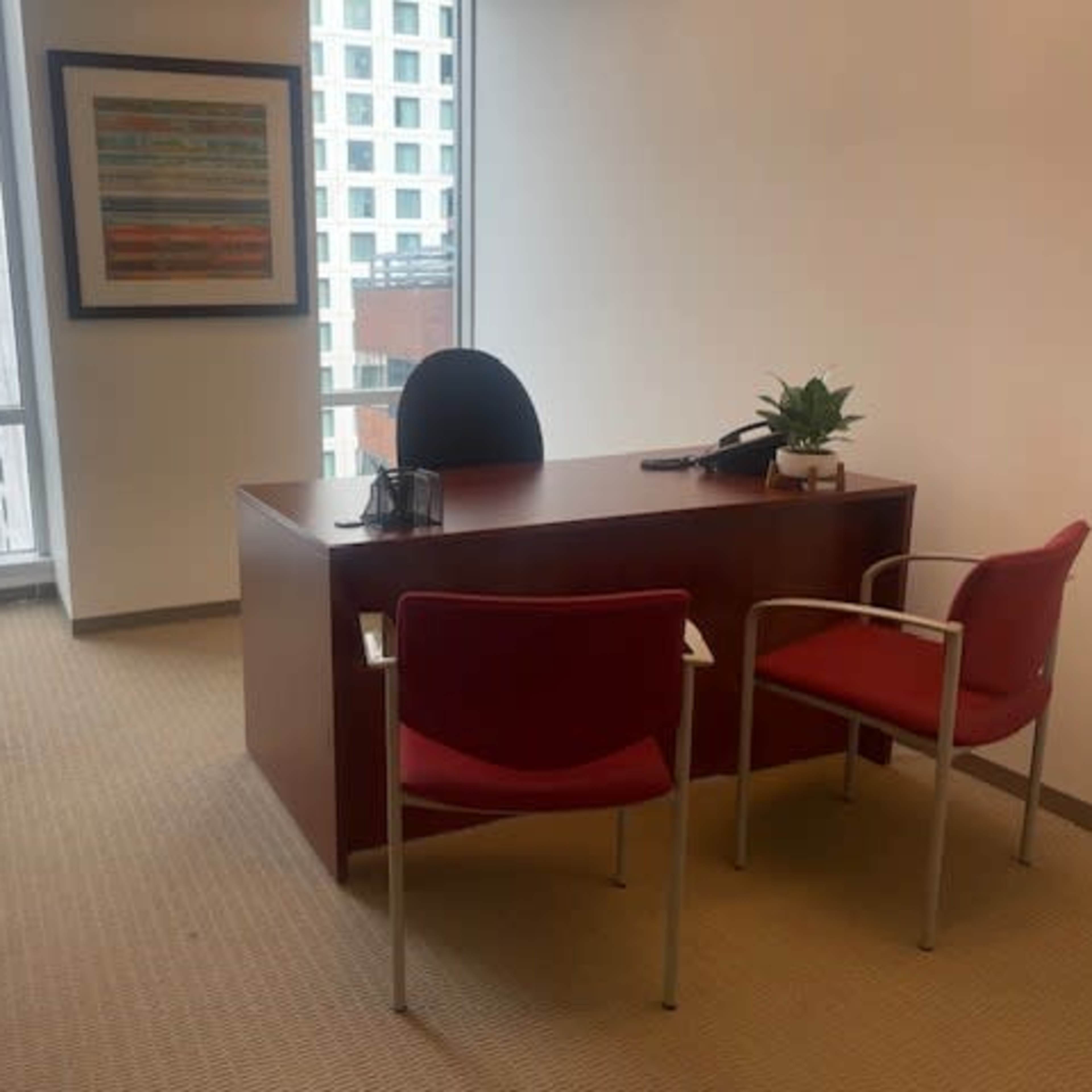A modern office features a wooden desk with a chair, two red client chairs, and a large window overlooking a cityscape.