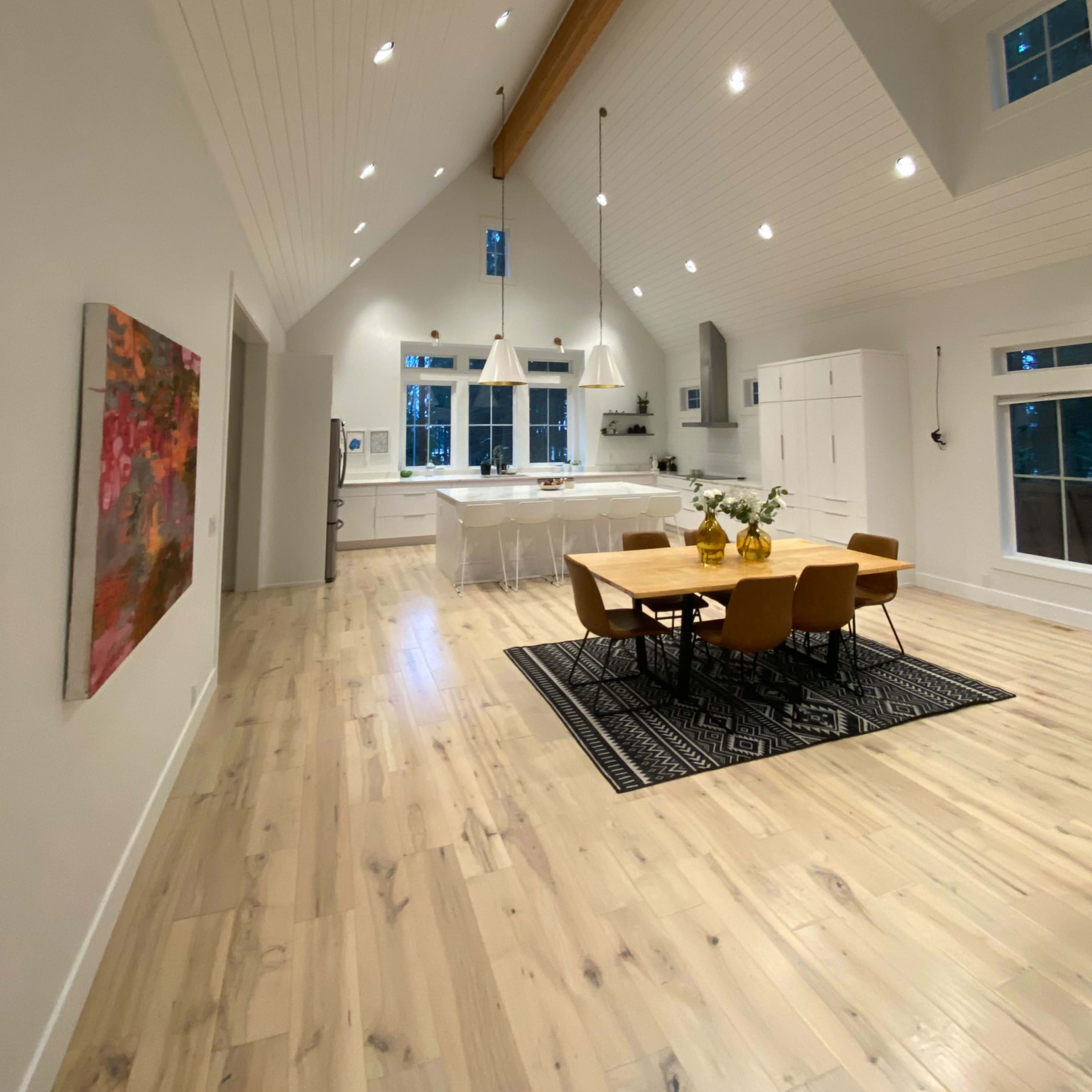 A spacious, well-lit kitchen and dining area with high ceilings, a wooden beam, and a modern dining table surrounded by yellow chairs.