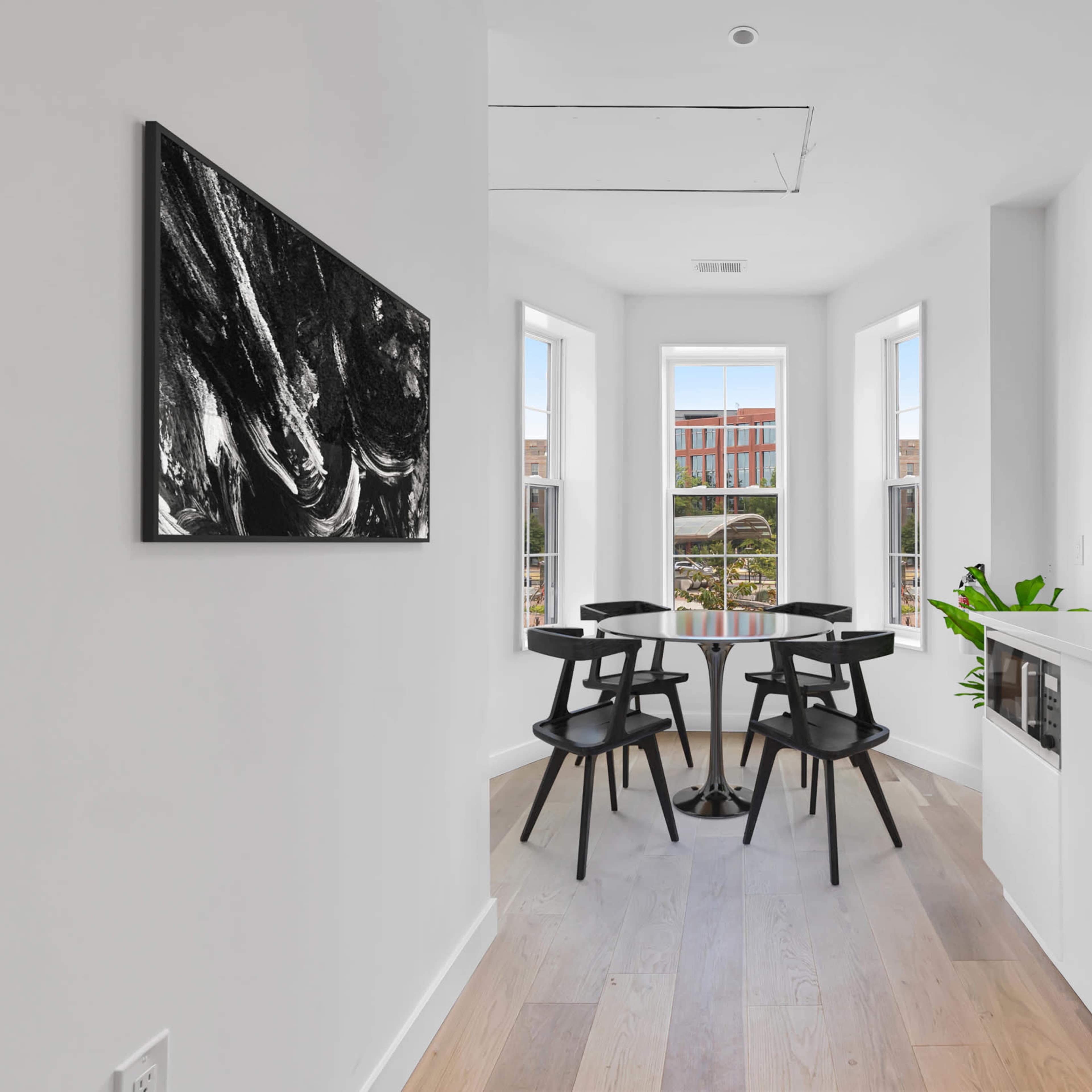 A small dining area features a round table with four black chairs, surrounded by large windows and a sleek kitchen with modern appliances.