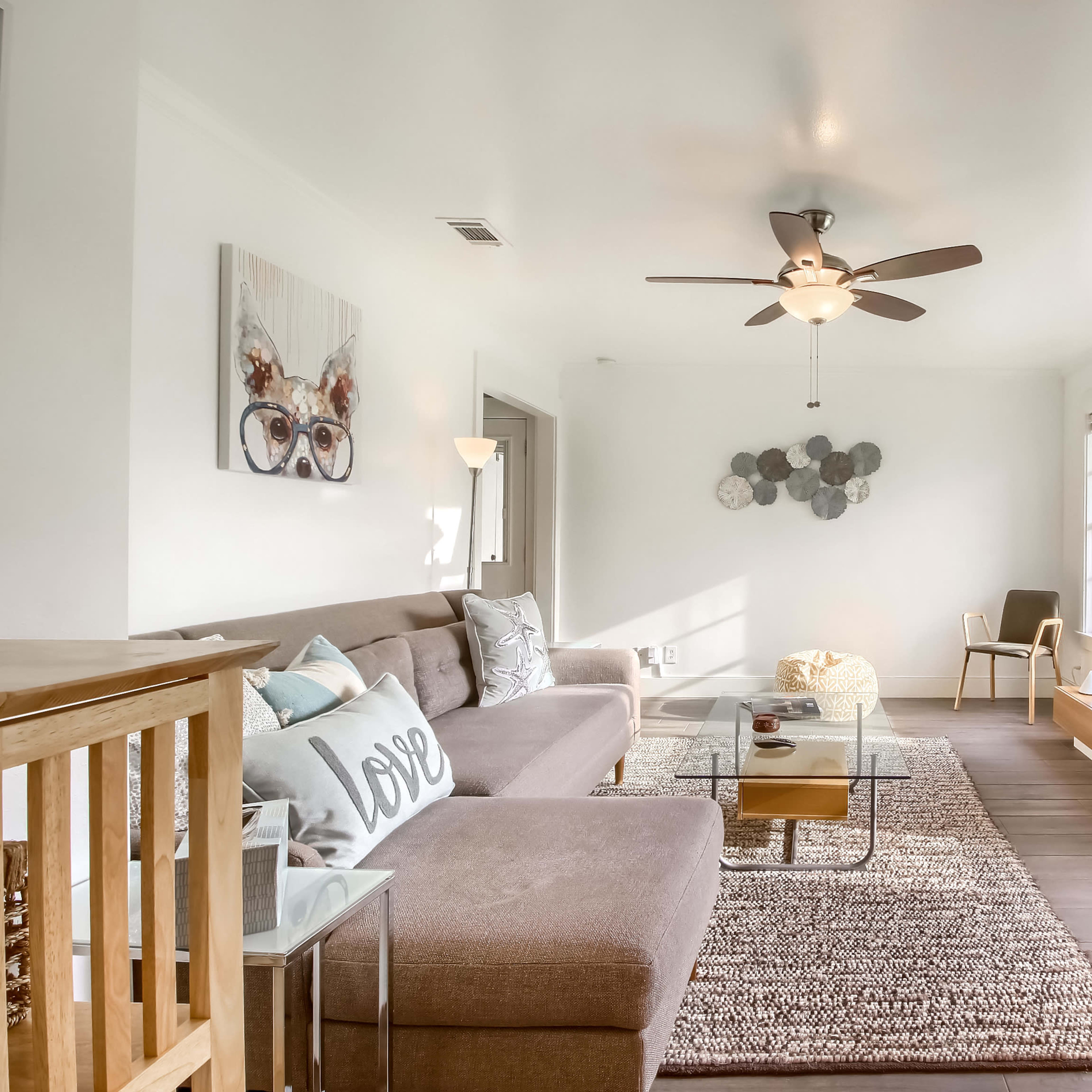 A bright, airy living room with a sectional sofa, a glass coffee table, and a large window overlooking greenery.