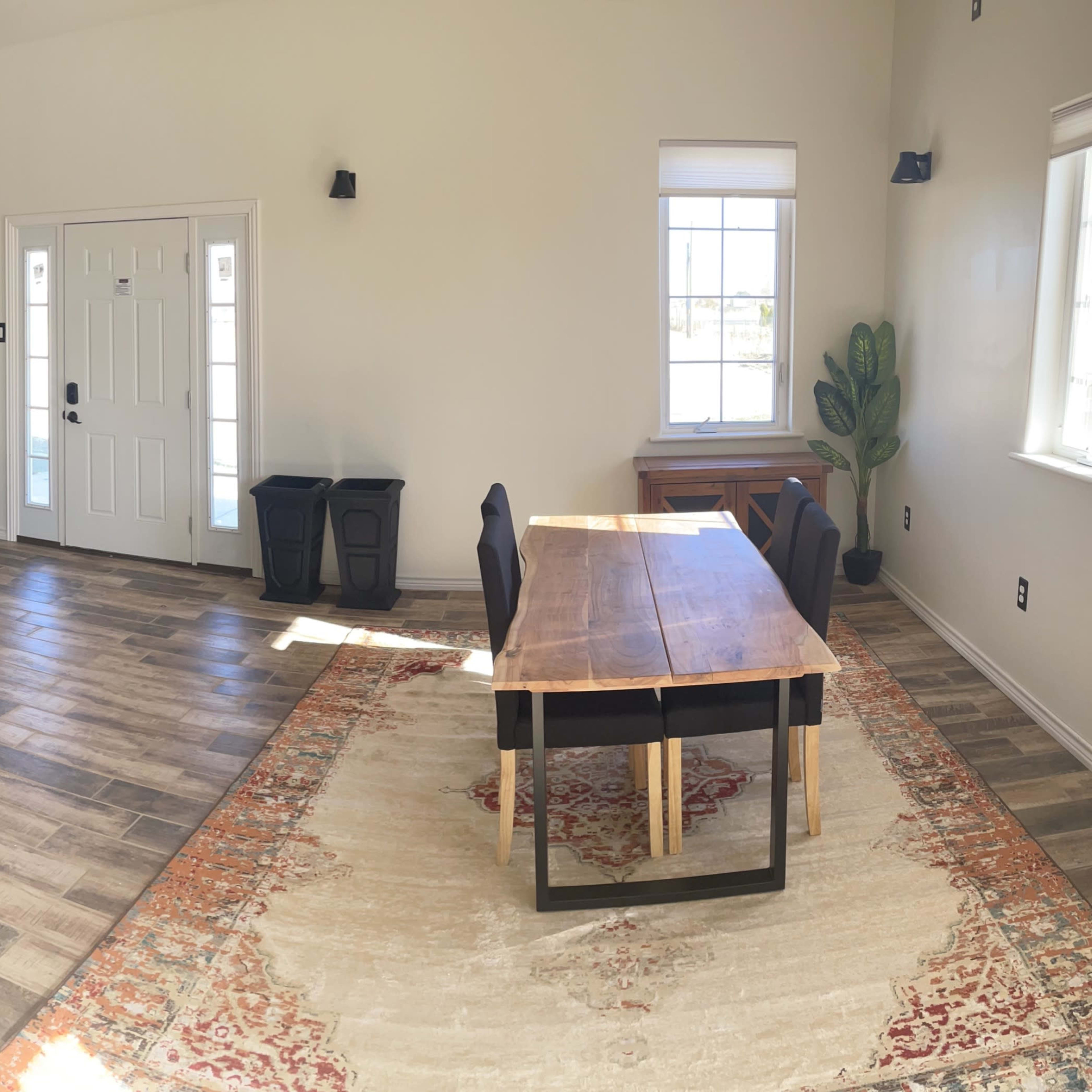 A spacious room with a wooden dining table, a couch, a small seating area, and large windows allowing natural light to enter.