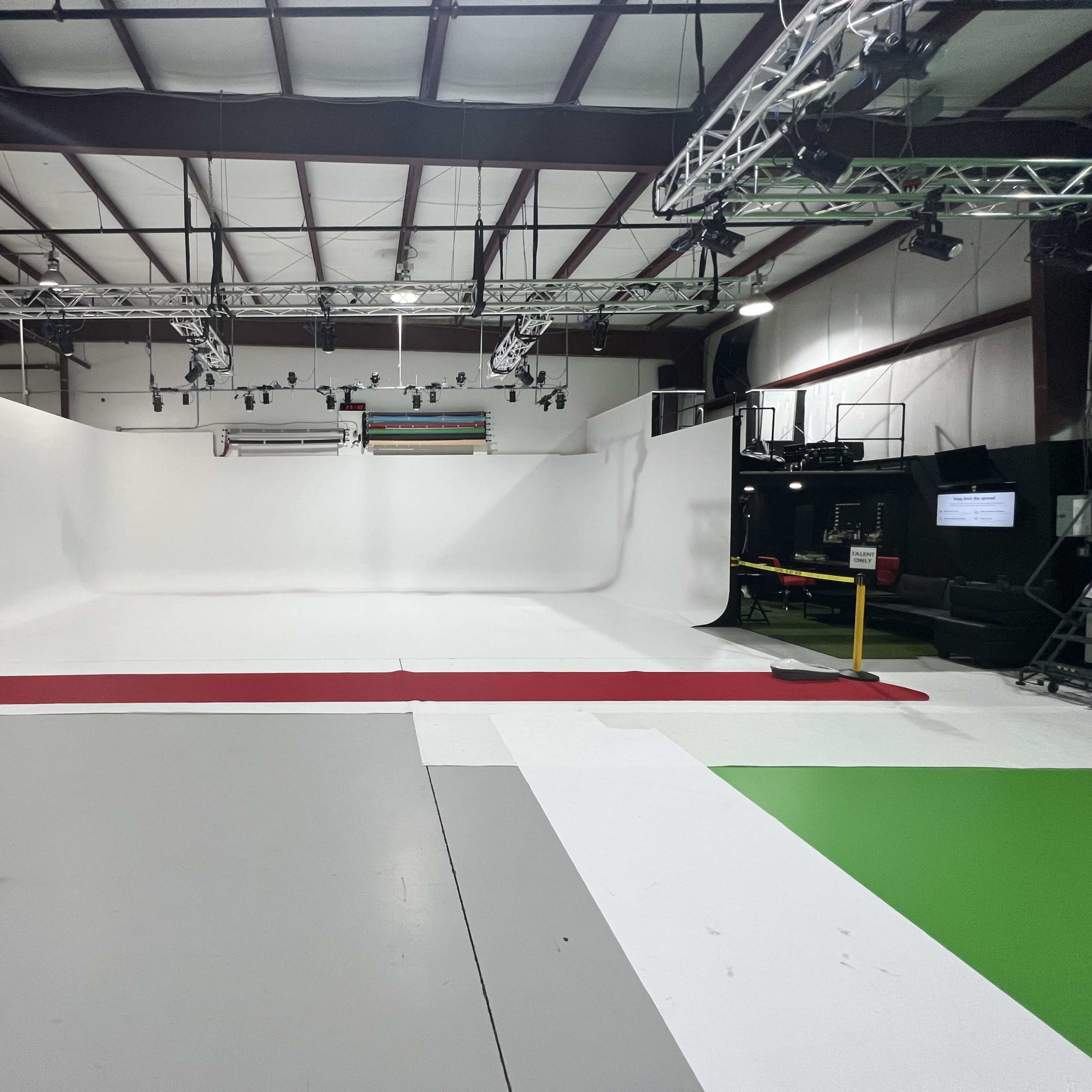 A spacious studio with a white backdrop and various lighting equipment, featuring a colored carpet and sections of different flooring.