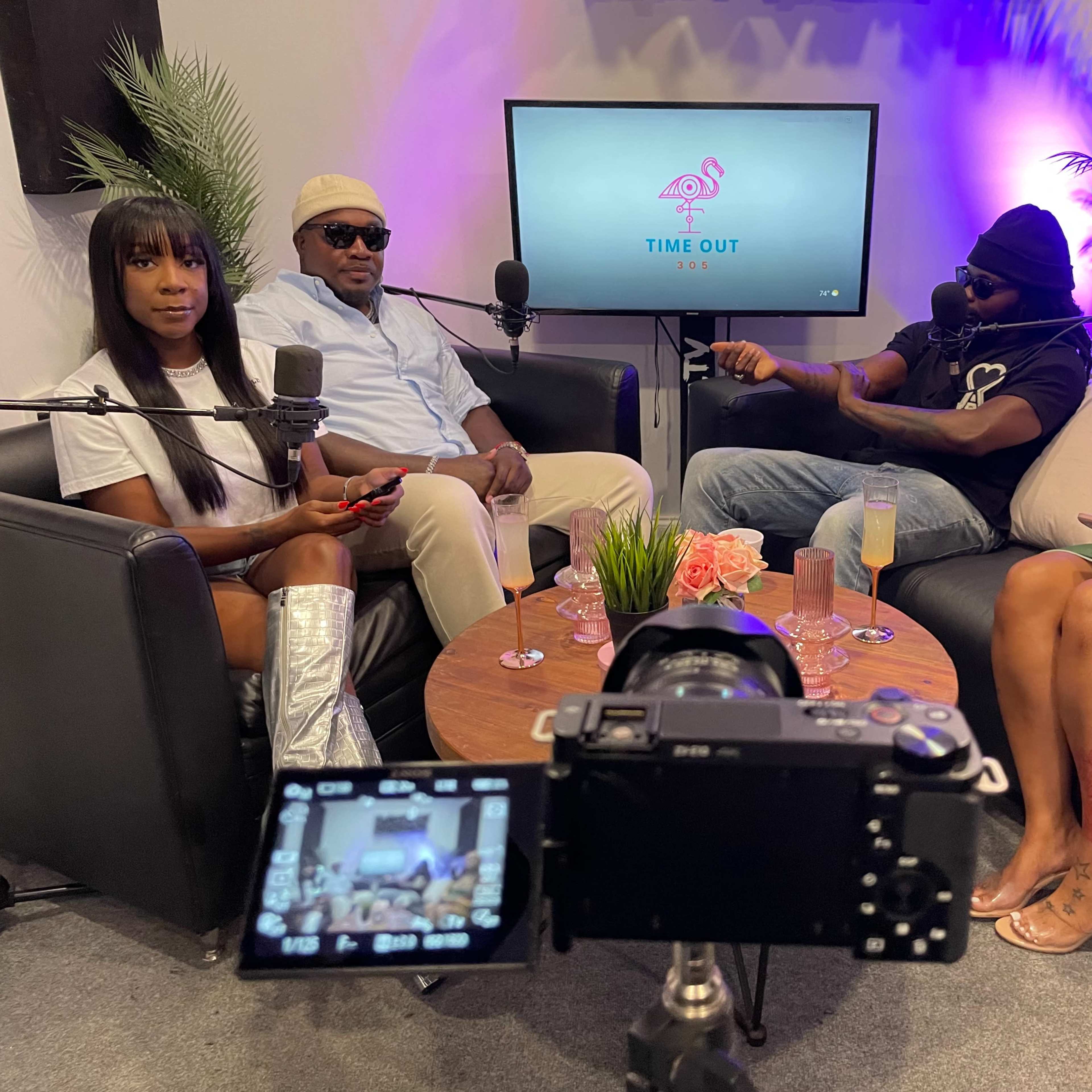 A group of four people sits on a set with microphones, preparing for a podcast recording.