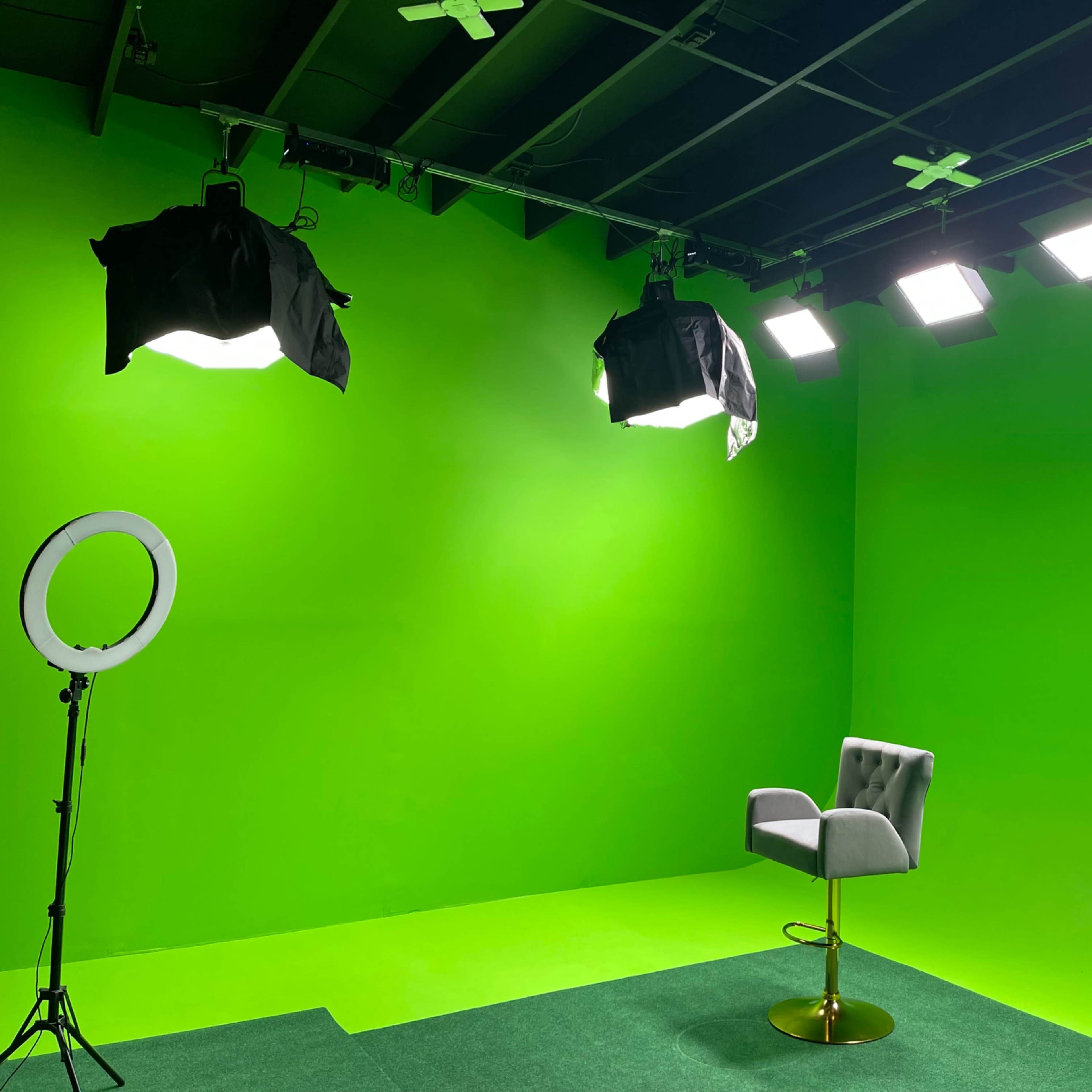 A green screen studio setup with a single chair, bright lighting, and a ring light on a stand.