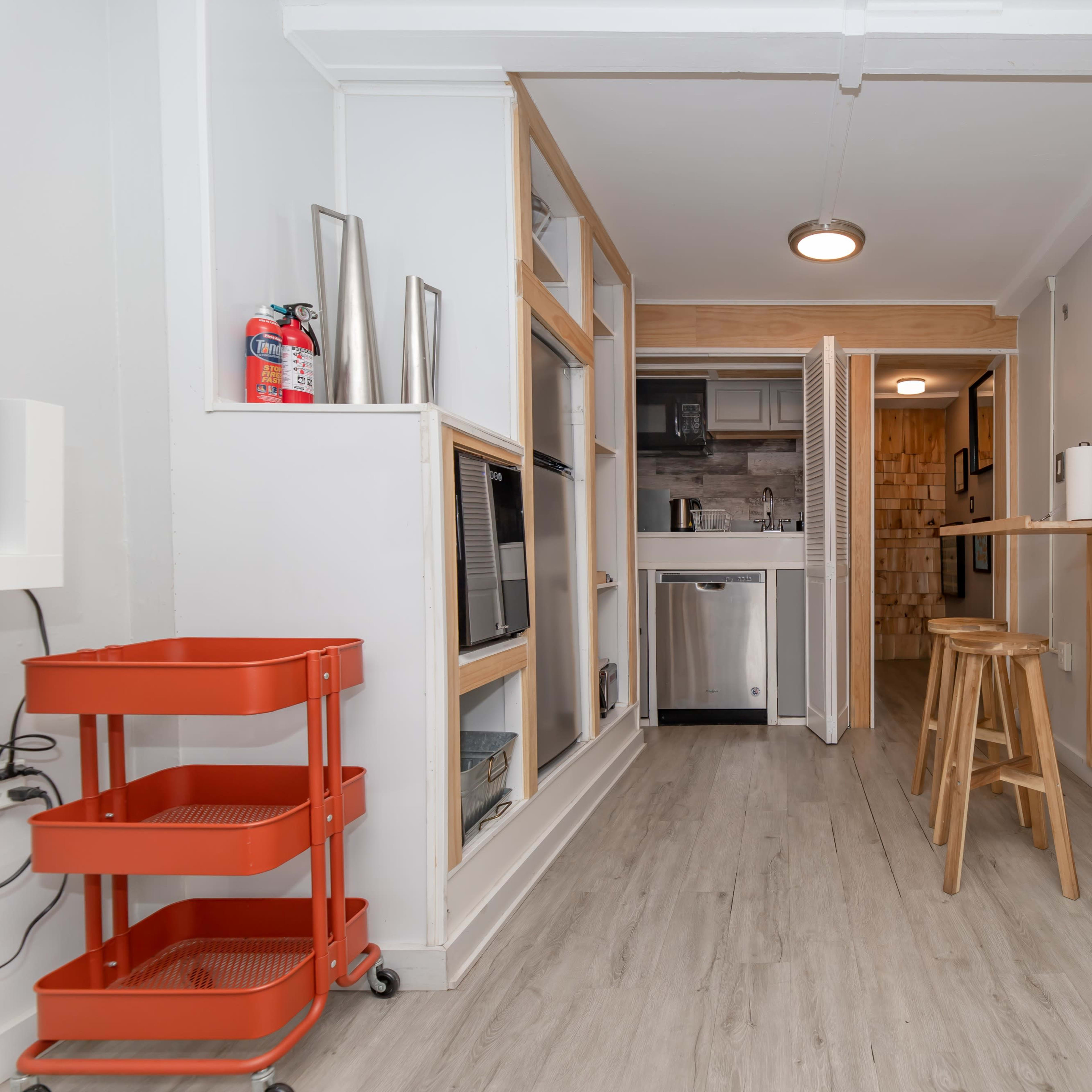 A compact kitchen area featuring wood accents, a bar stool, and a sliding door leading to another room.