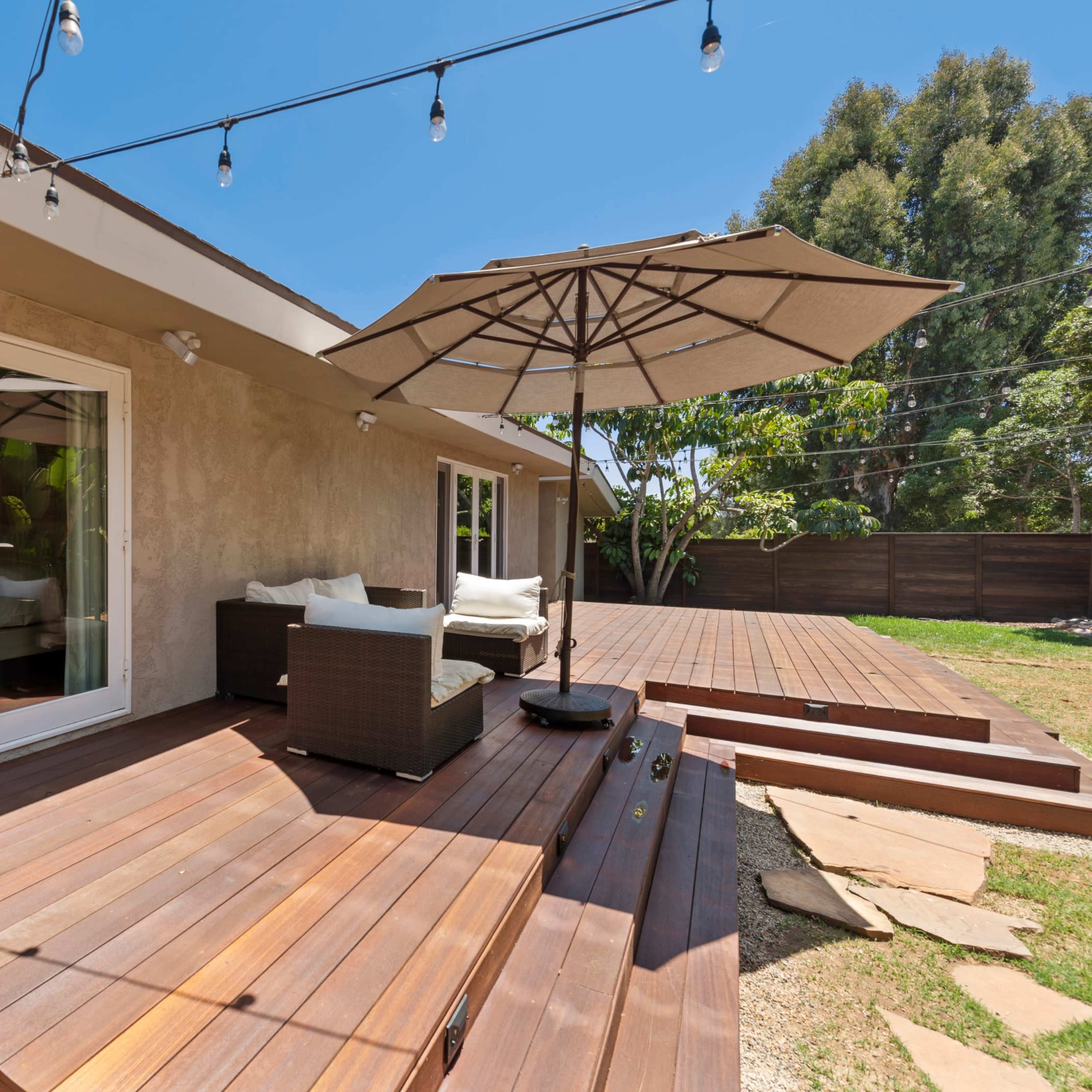 A wooden deck with a patio umbrella and outdoor seating adjacent to a house.