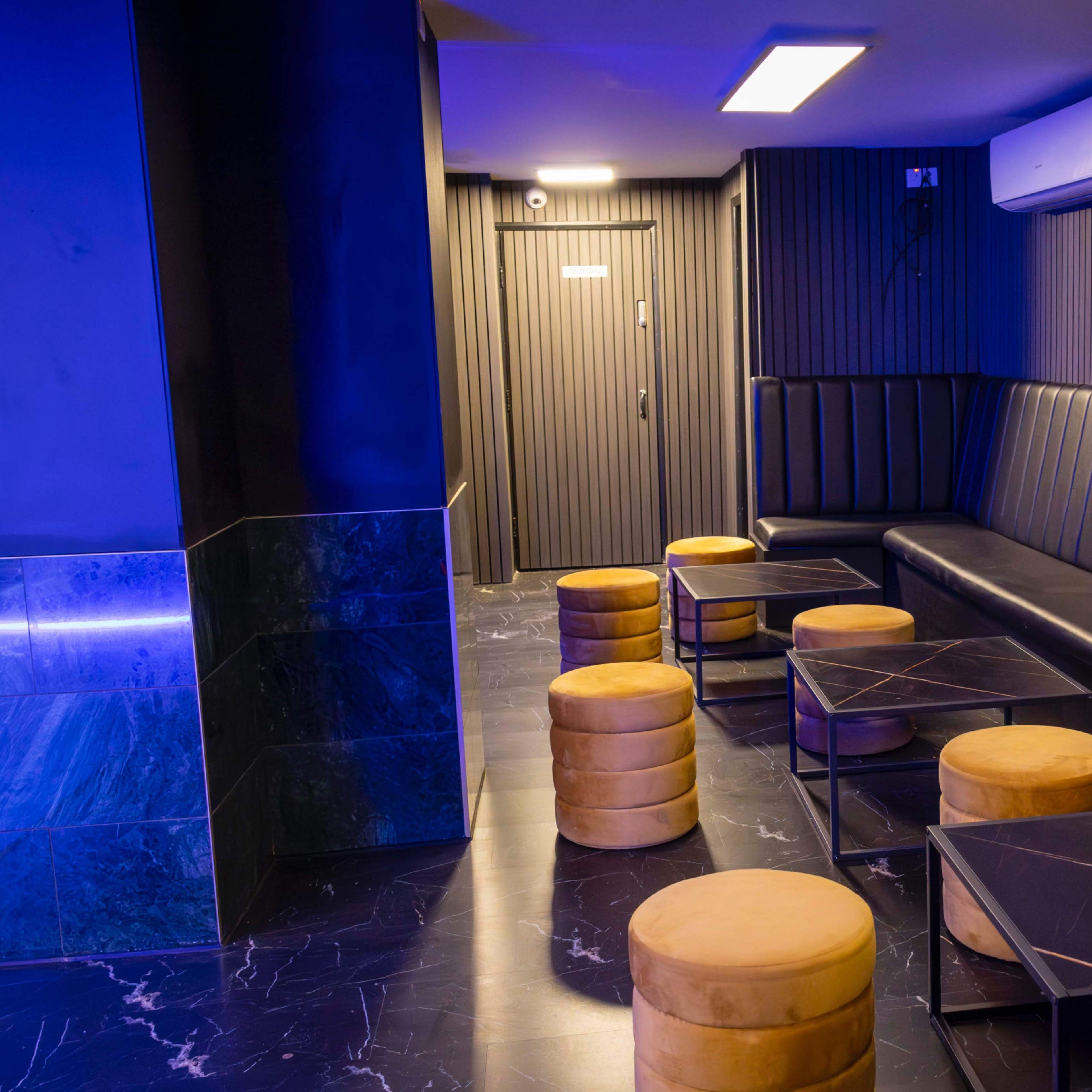 A modern lounge area with black leather seating, round wooden stools, and black marble-topped tables against a textured wall.