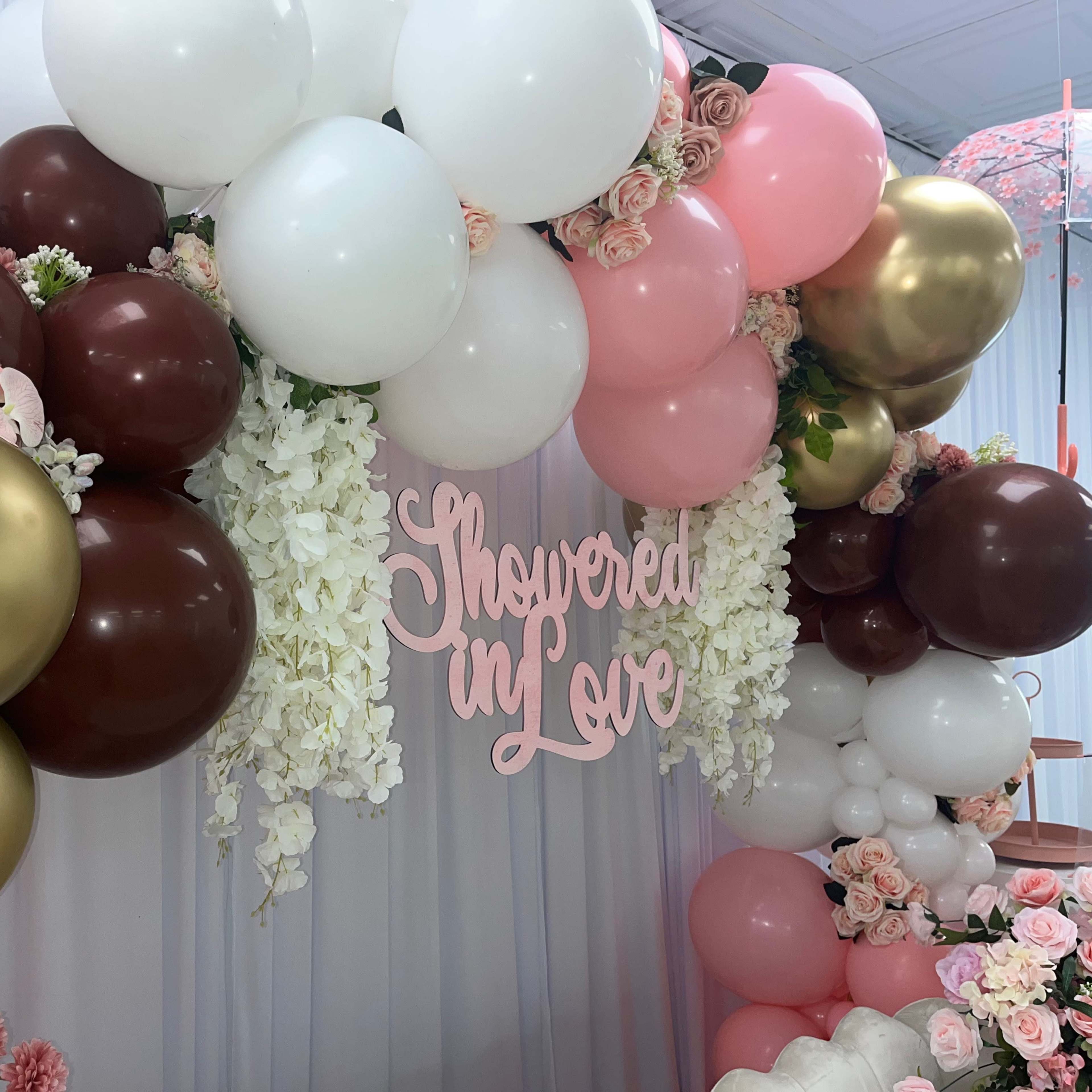 A decorative arch made of balloons in various colors, adorned with flowers and a sign that reads "Showered in Love."