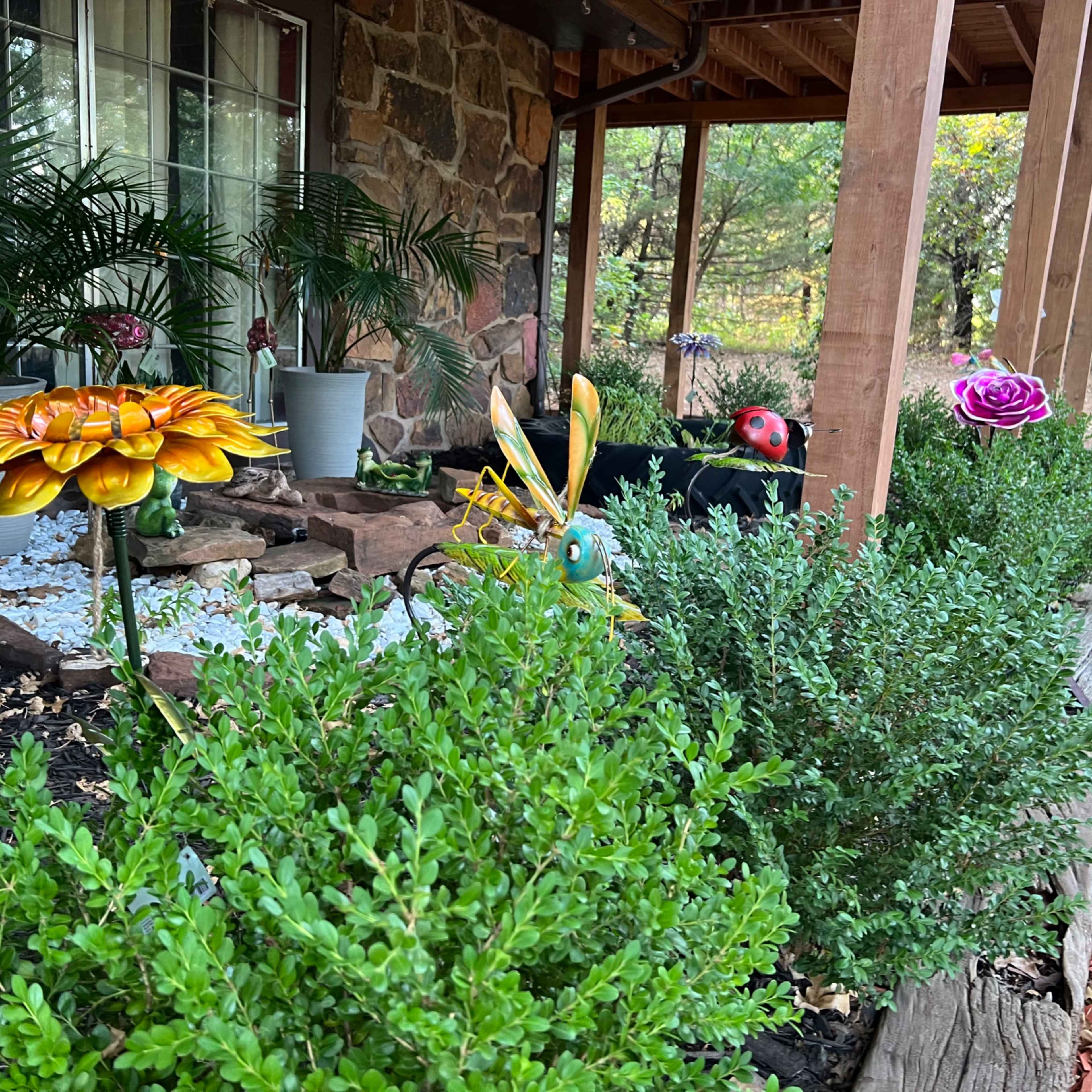 A garden area featuring colorful artificial flowers and greenery near a stone-patterned house.