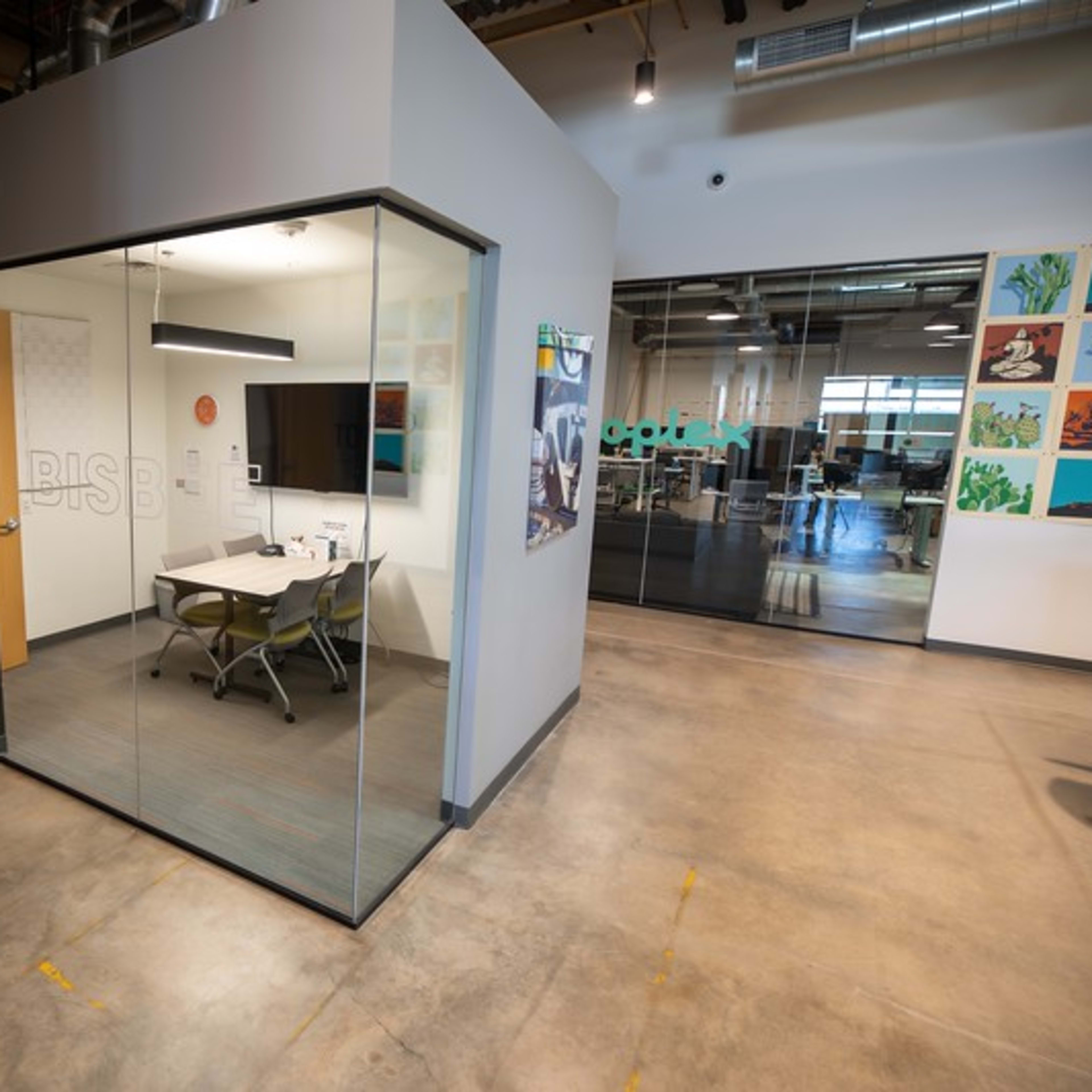A modern office space with a glass-walled meeting room featuring a table and chairs.
