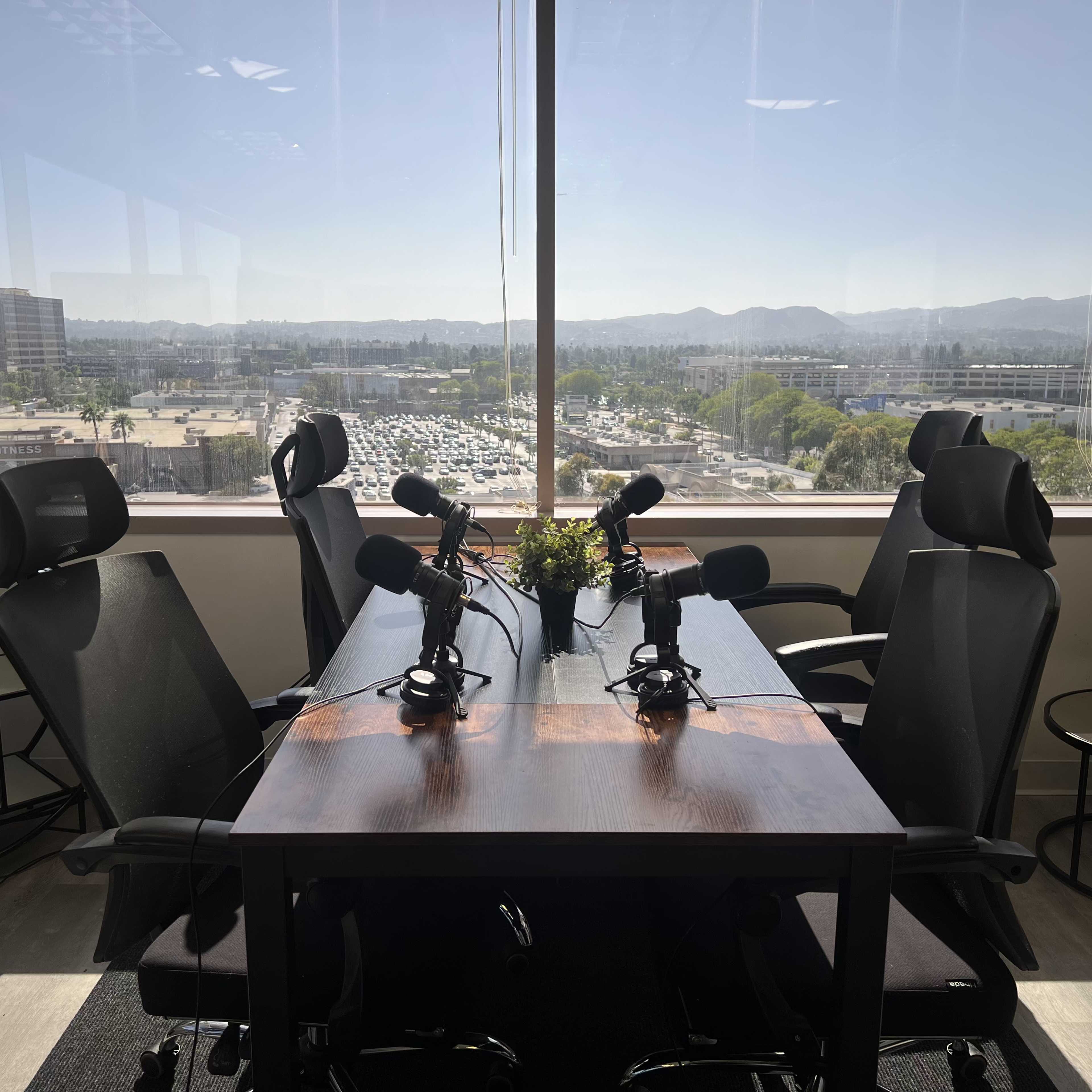A modern conference room with a large table and microphones set up for discussions, offering a view of buildings and mountains outside the window.