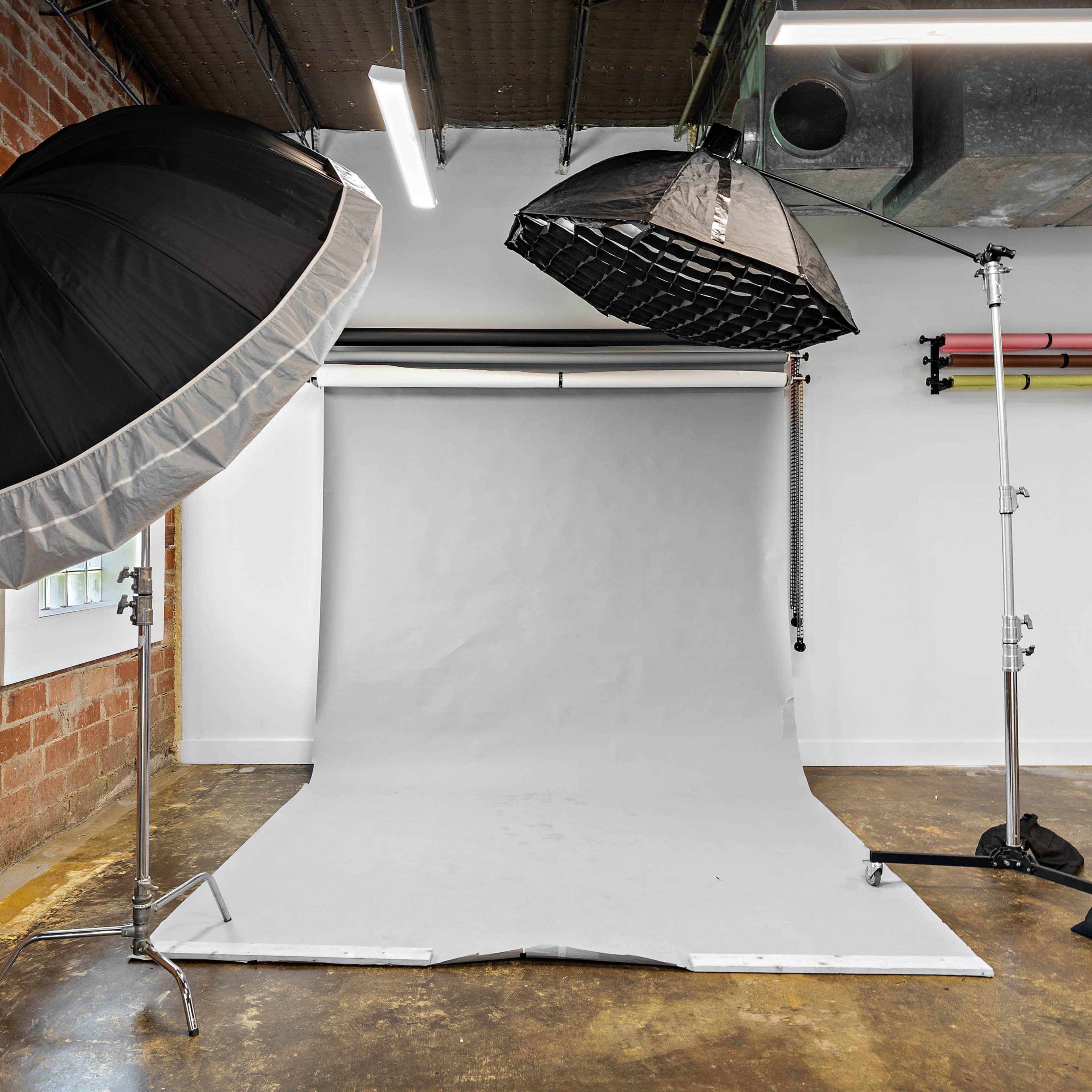 A photography studio with three softbox lights positioned over a gray backdrop on a polished concrete floor.