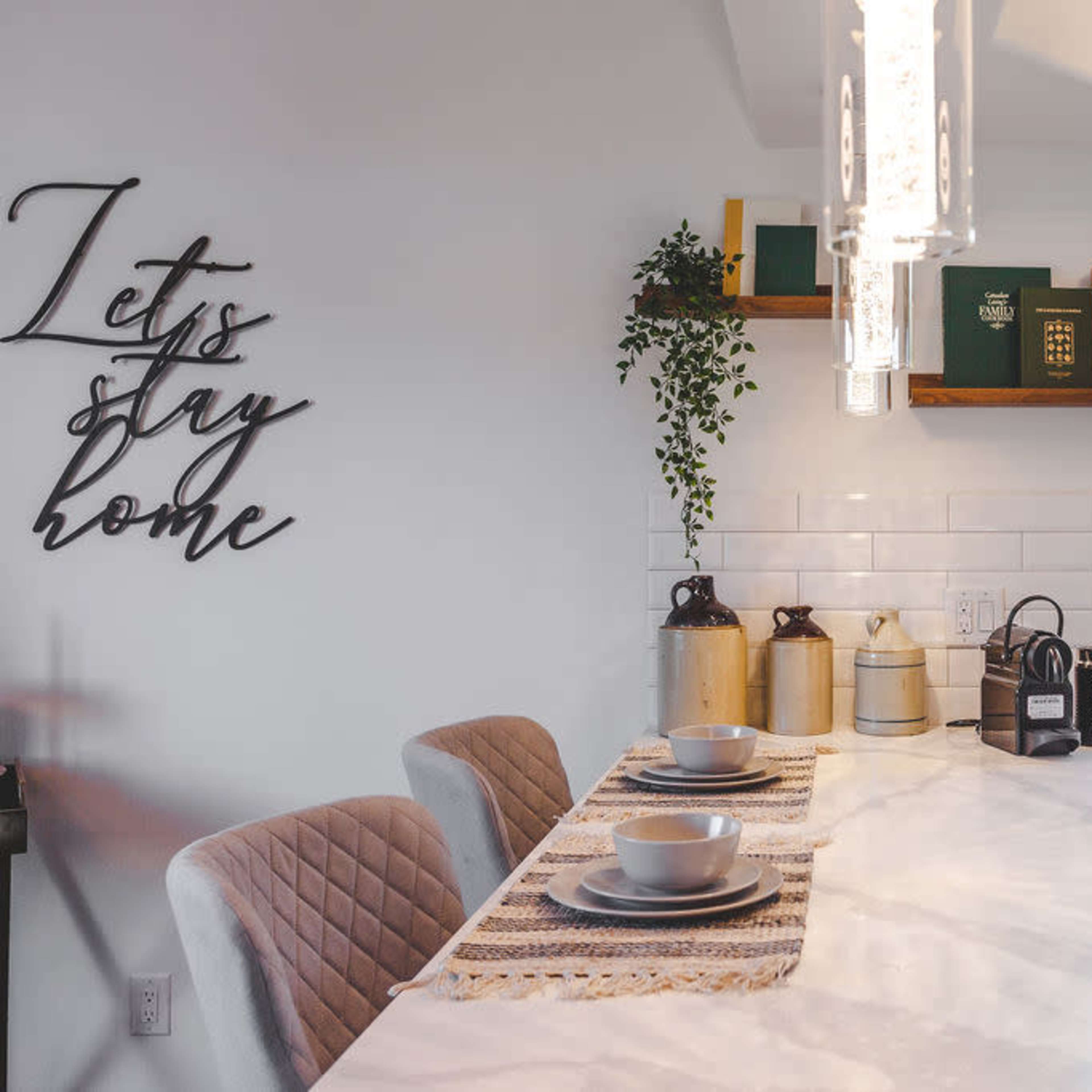 A modern kitchen features a marble countertop with two place settings, decorative canisters, and a window overlooking greenery.