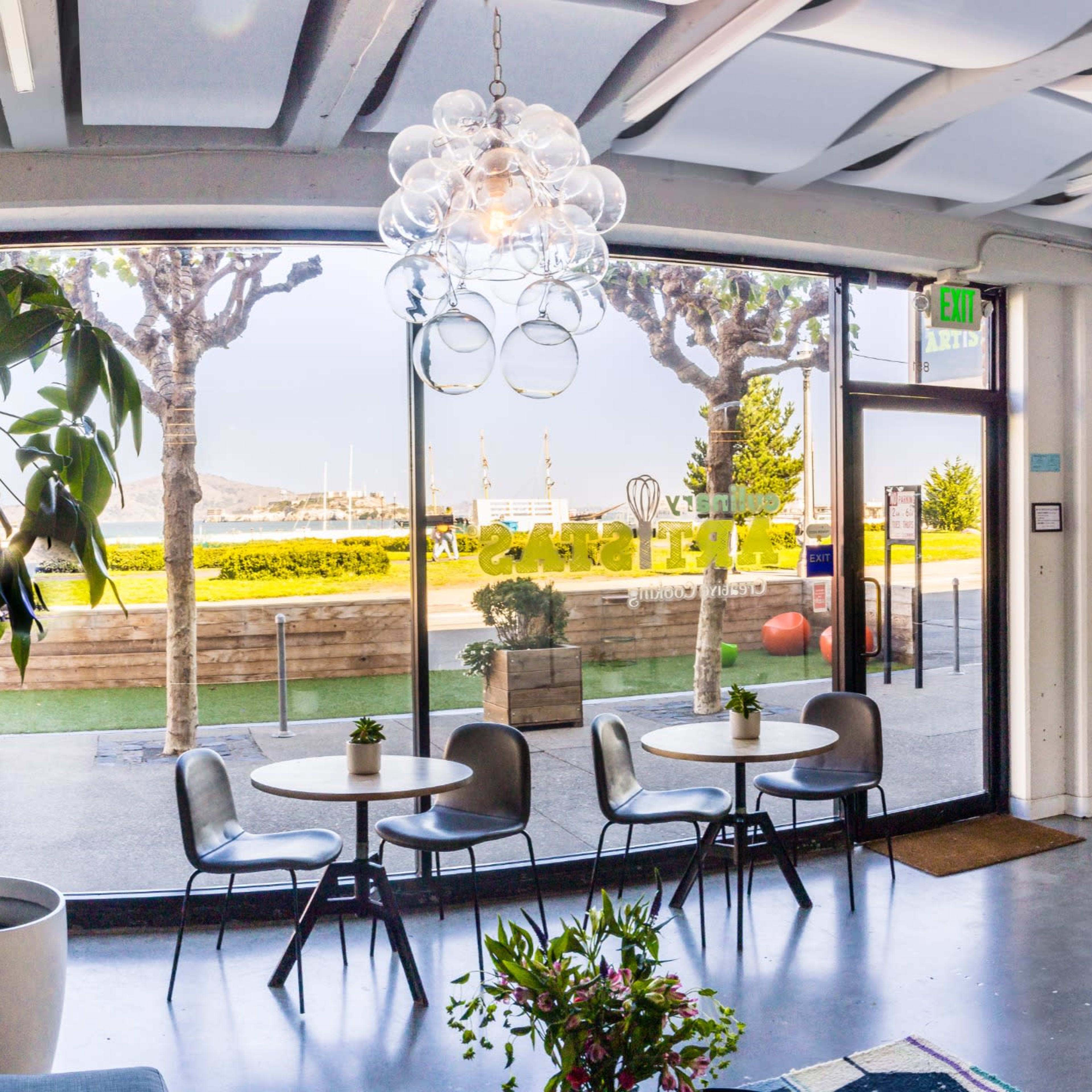 A modern interior space with large windows overlooking a landscaped area, featuring a seating area, a round mirror, and decorative plants.