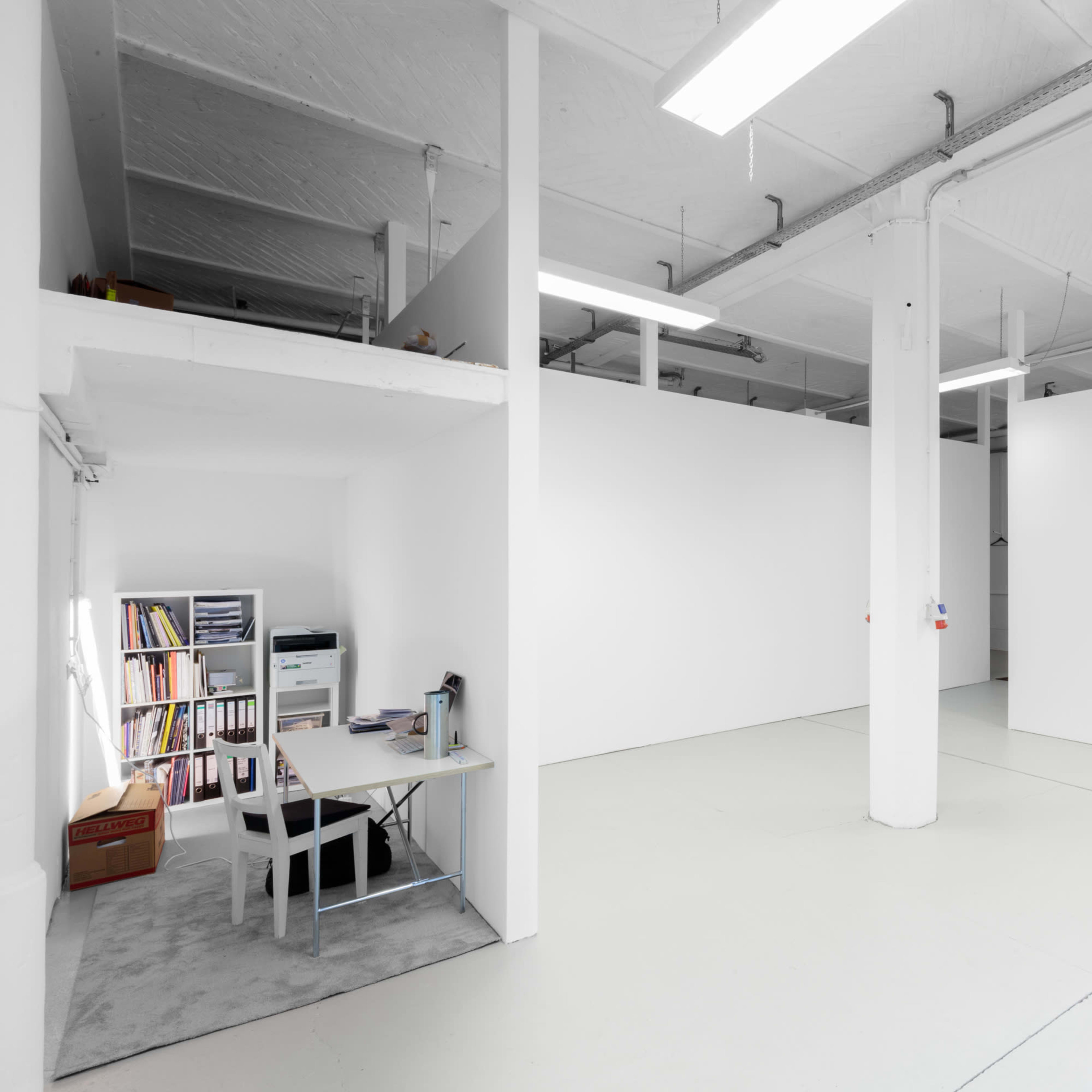 A spacious, minimalist open office with white walls and a desk arrangement in one corner.