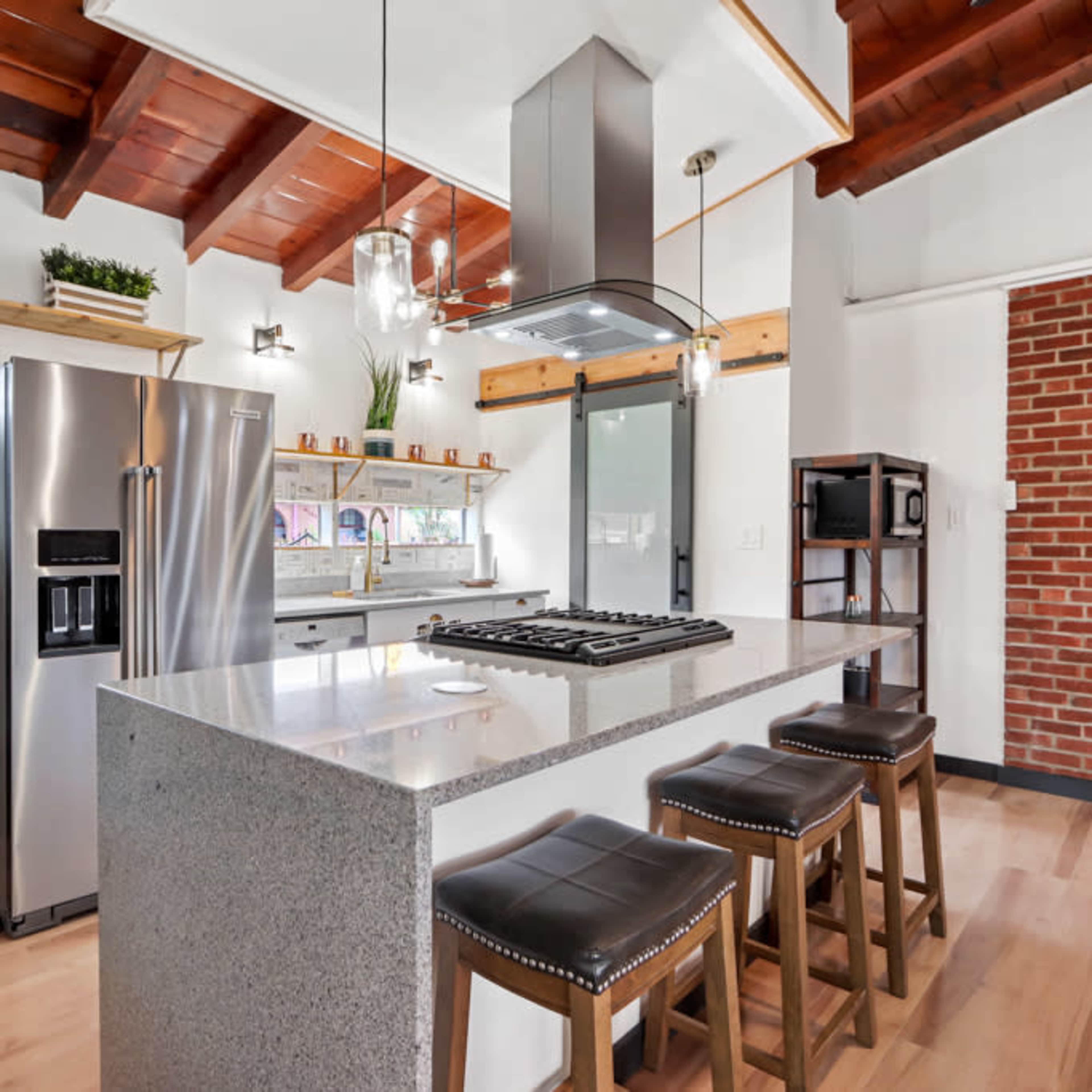 A modern kitchen with a large island, stainless steel appliances, and exposed wooden beams on the ceiling.