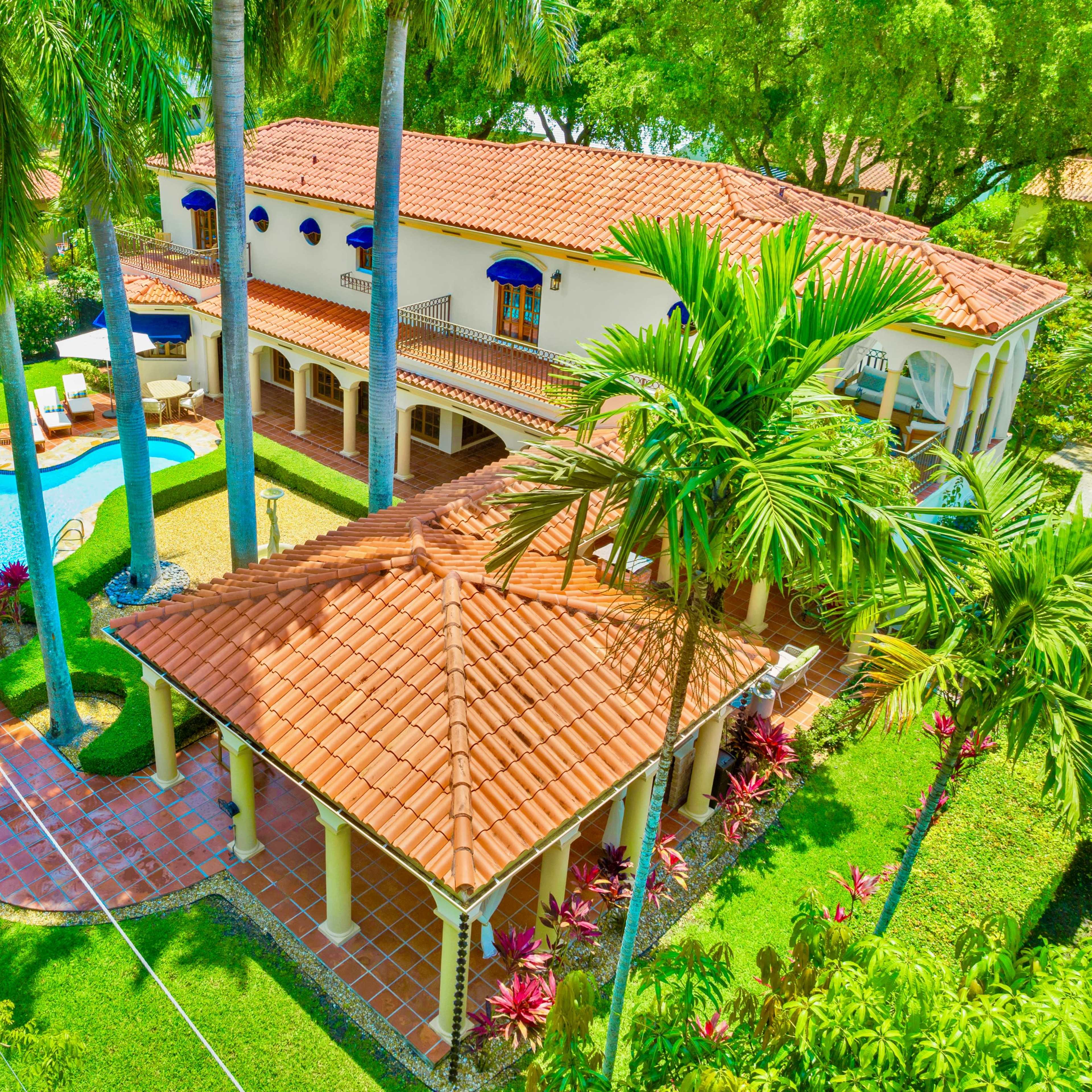 A spacious villa surrounded by palm trees, featuring a swimming pool and a separate gazebo with a tiled roof.