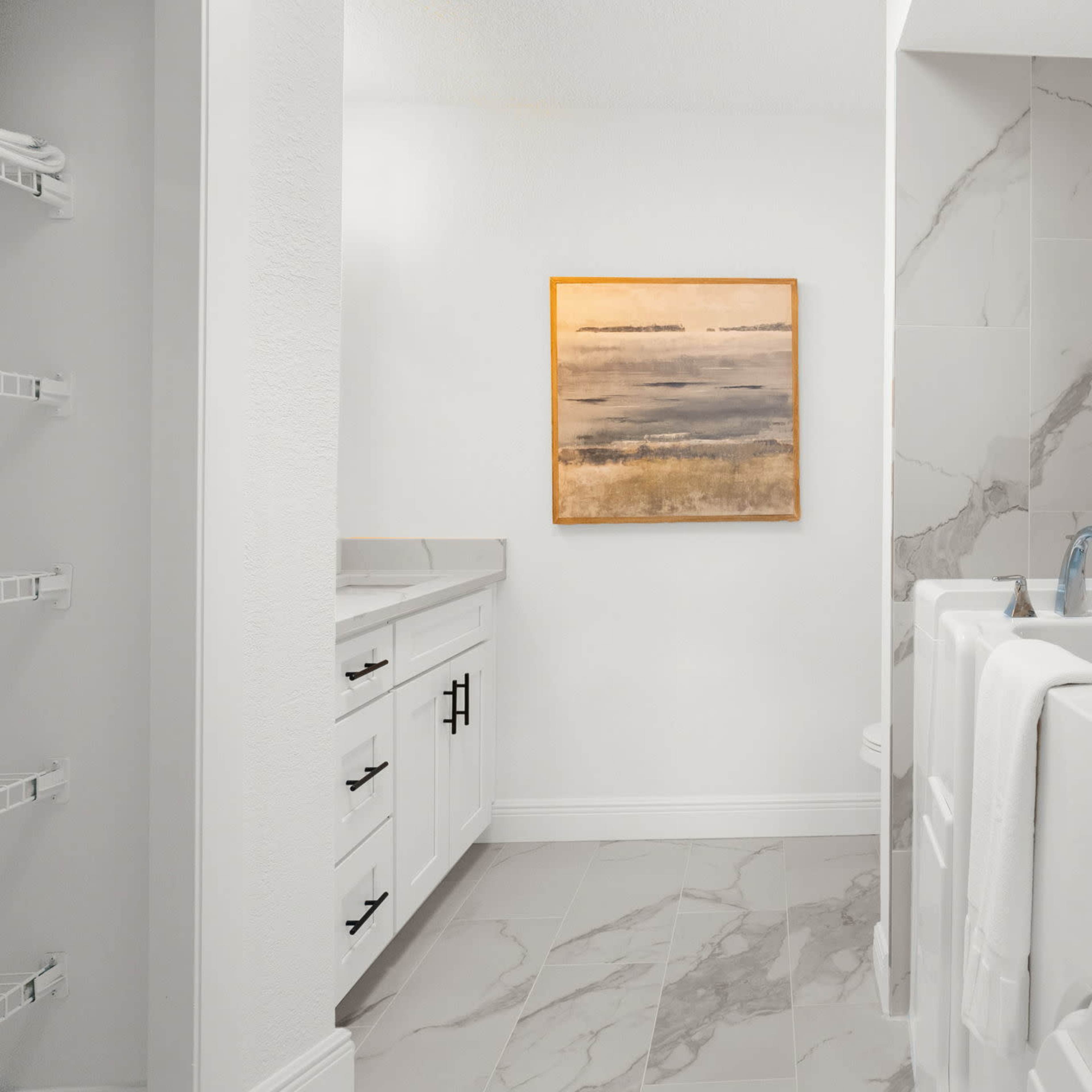 A modern bathroom with a walk-in bathtub, a sink area, and a piece of abstract art on the wall.