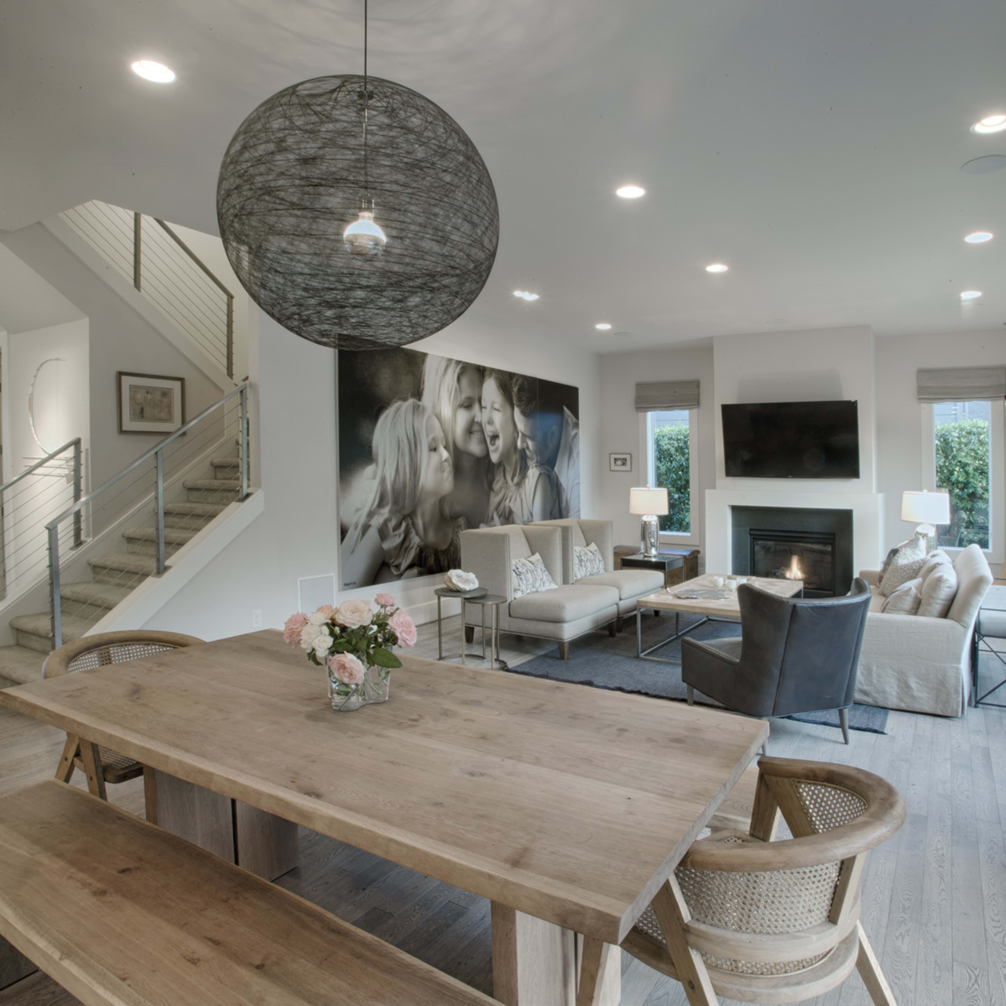 A modern, open-concept living room and dining area featuring a large dining table, comfortable seating arrangements, a fireplace, and a large wall mural.