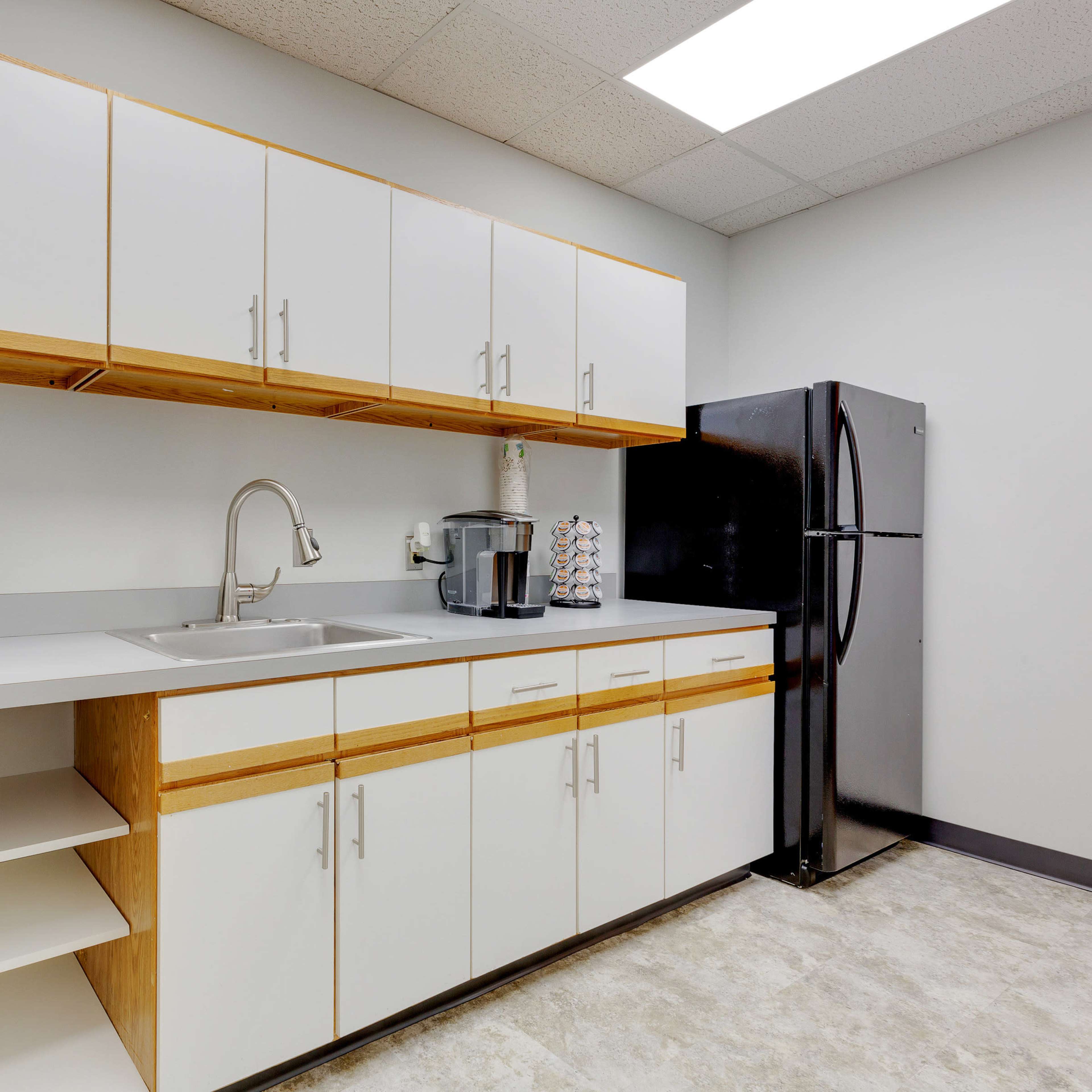 A kitchen area with white cabinets, a black refrigerator, a microwave on the countertop, and a sink.