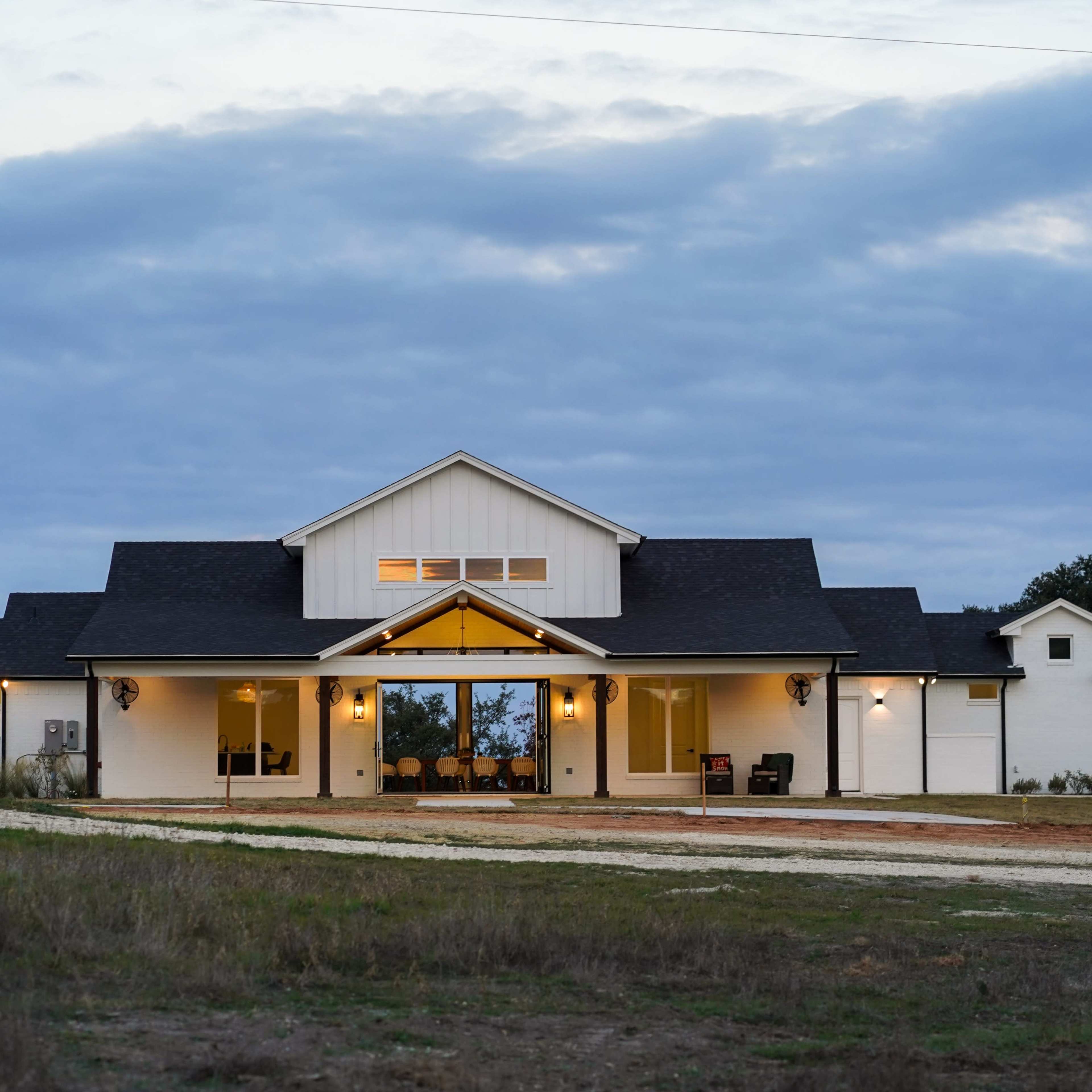 A modern house with a white exterior and a large front porch is set against a cloudy sky.