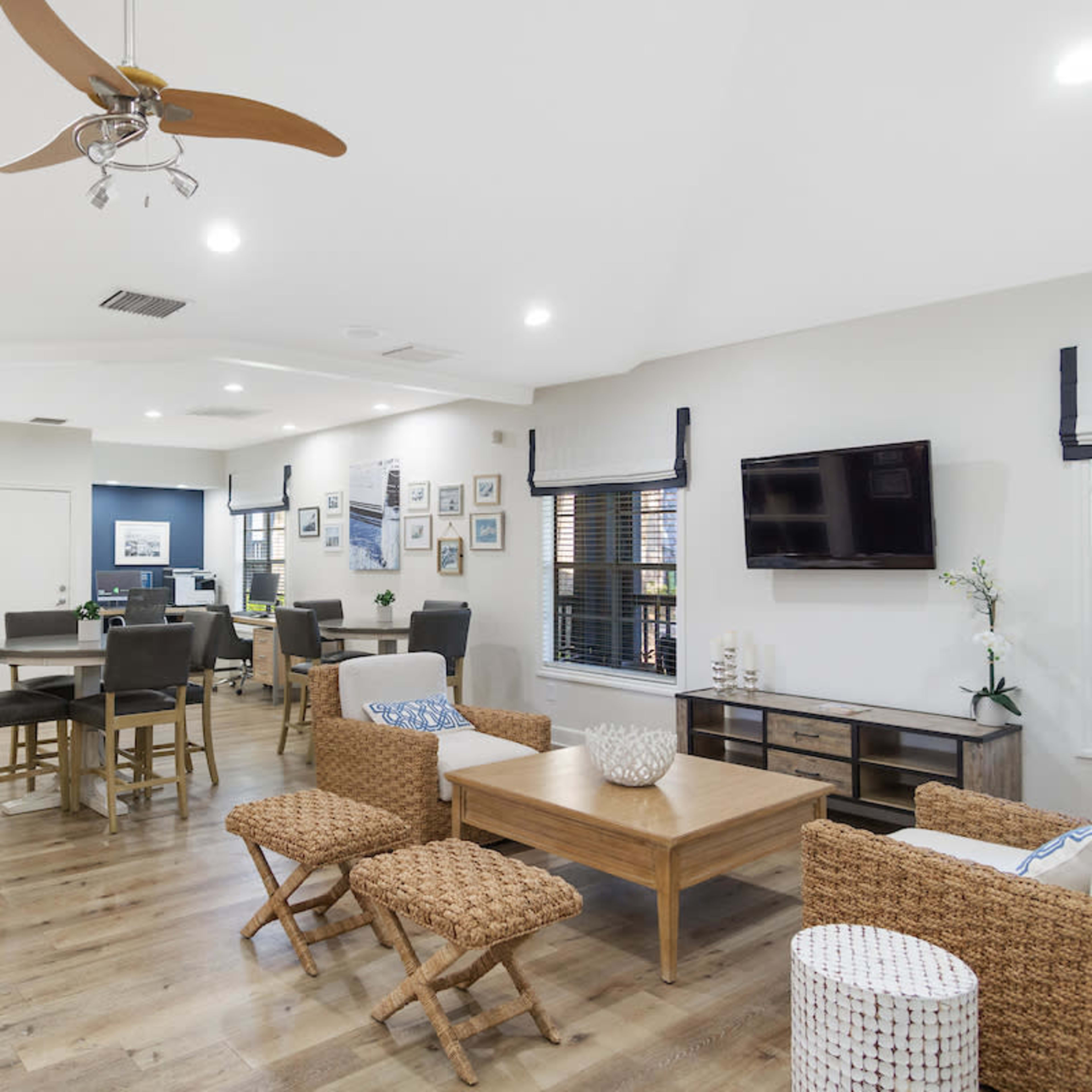 A modern, open living and dining area with a wooden floor, seating arrangements, a dining table, and a wall-mounted TV.