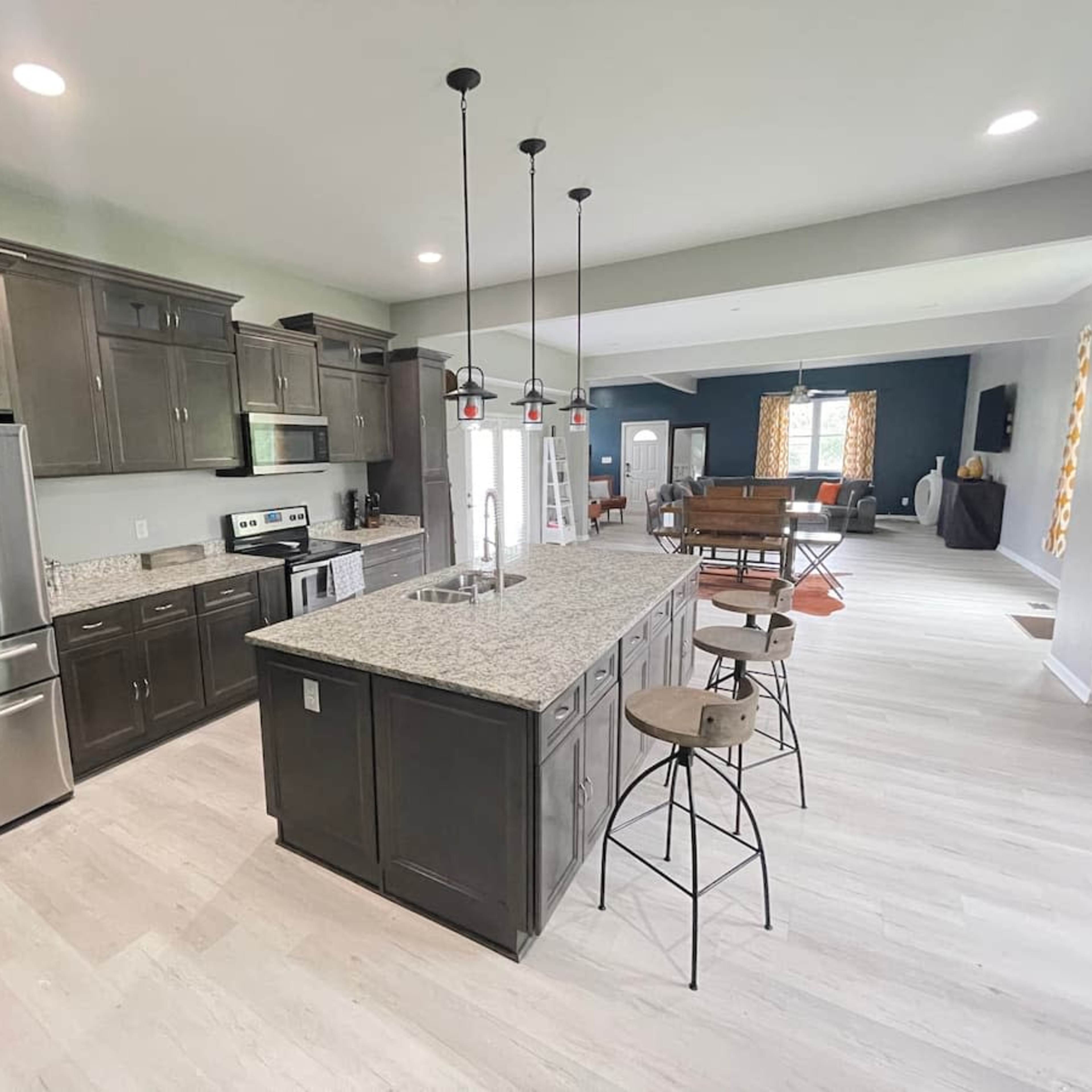 A modern kitchen with dark wooden cabinets, a large island with bar stools, and stainless steel appliances, all illuminated by overhead pendant lights.