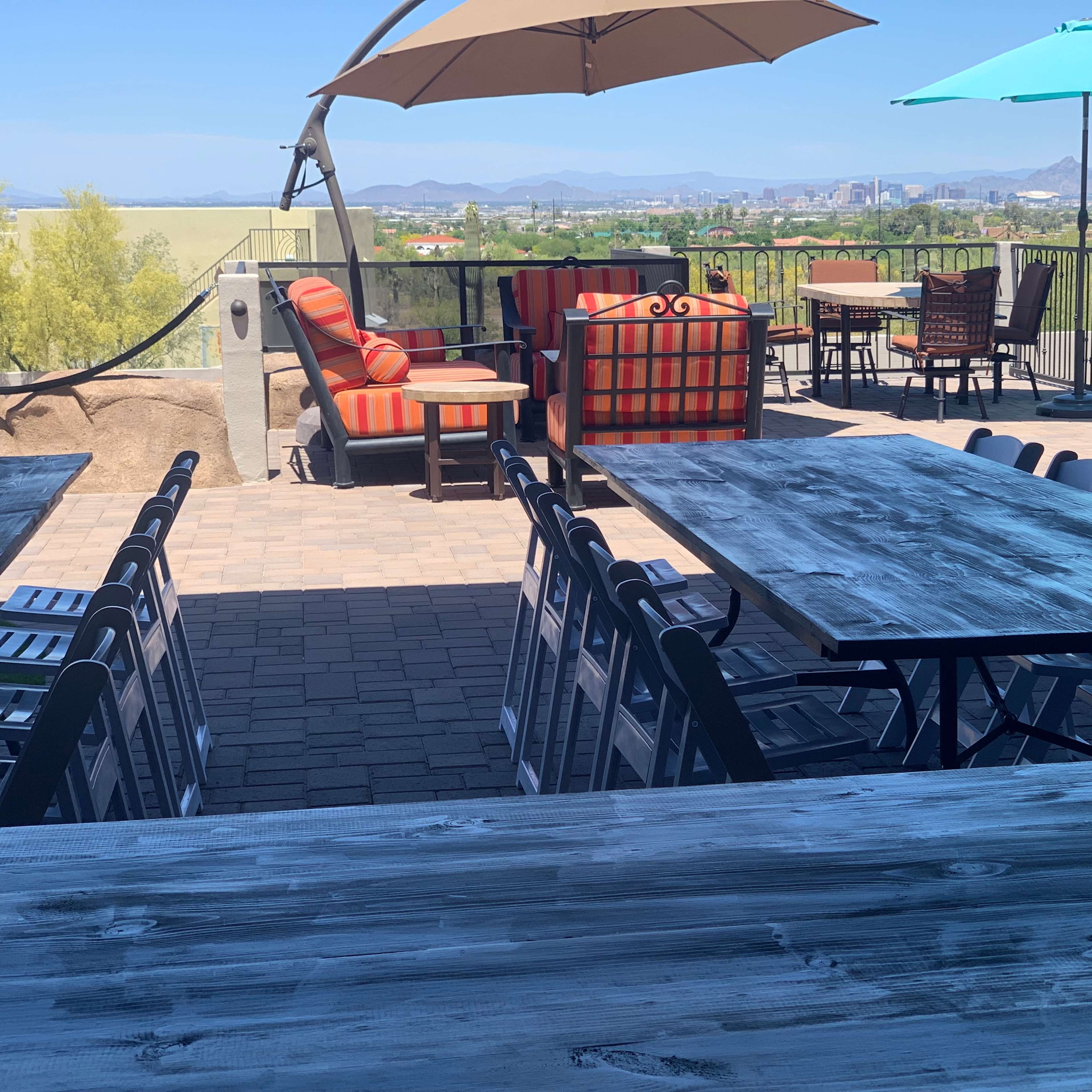 A spacious outdoor patio features several tables and chairs, colorful seating areas, and a view of distant mountains and cityscape.