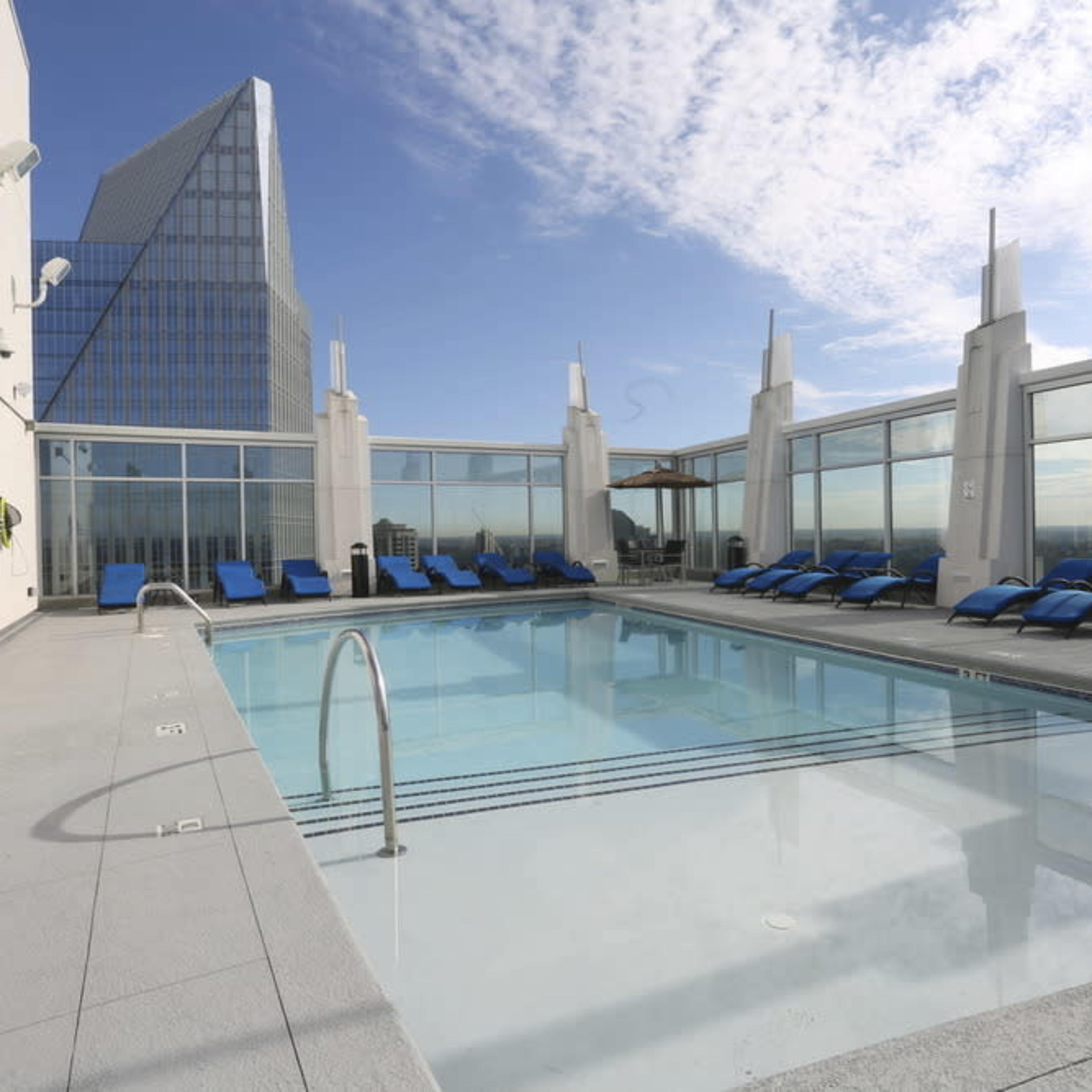 A rooftop pool area with lounge chairs and a panoramic view of the skyline.