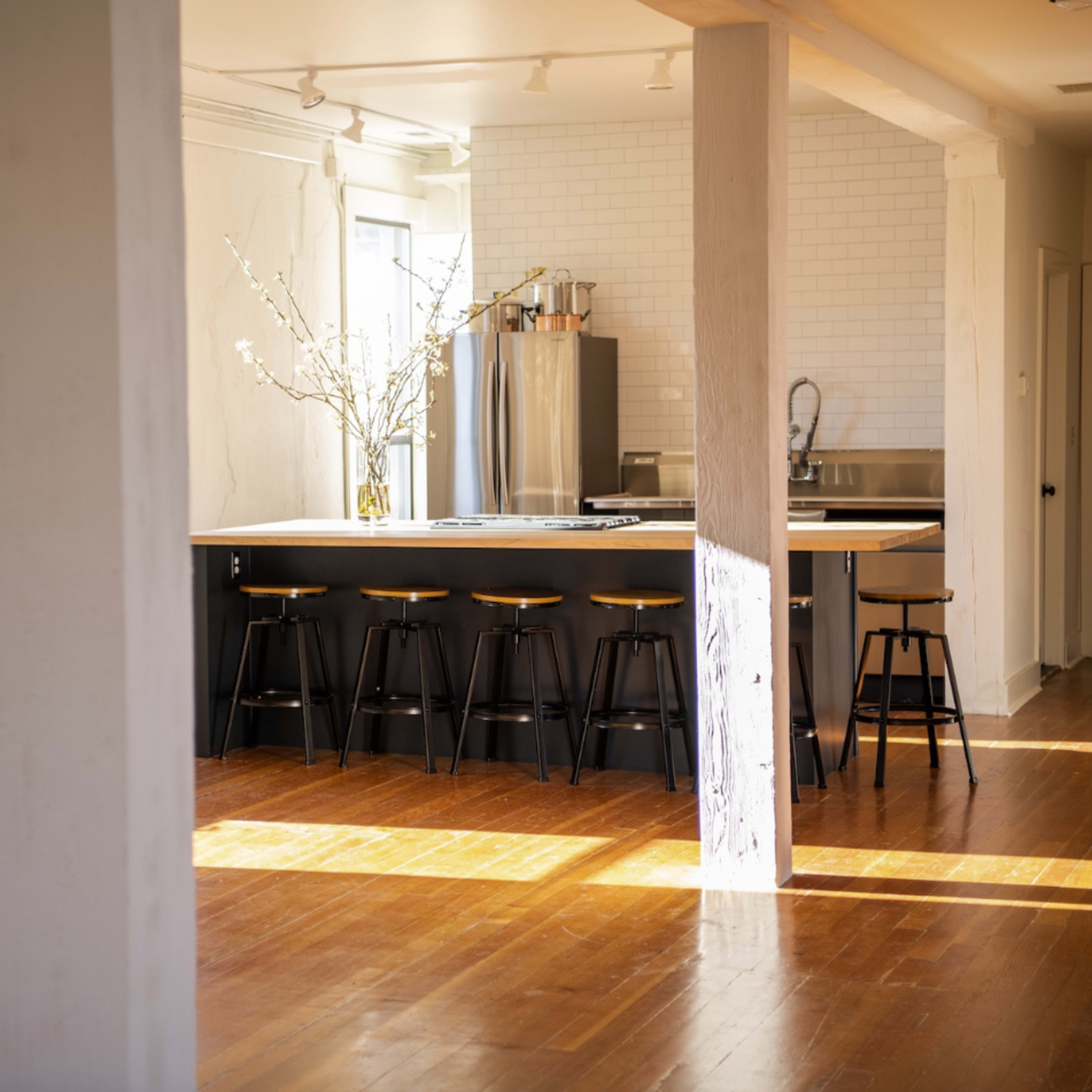 A spacious, modern kitchen with a large island, a line of stools, and natural light streaming through large windows.