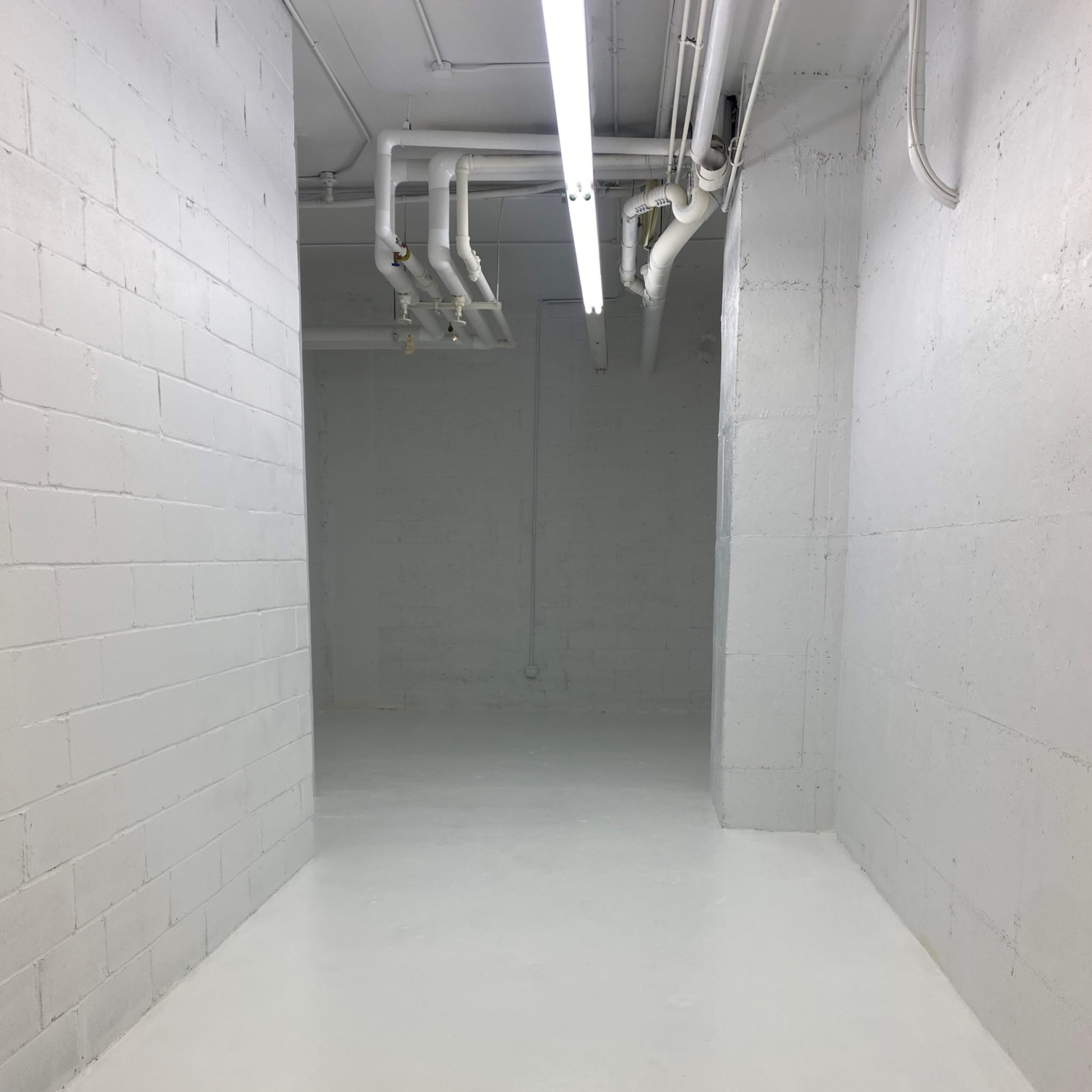 A long, empty corridor in a basement with gray concrete walls and a polished white floor.