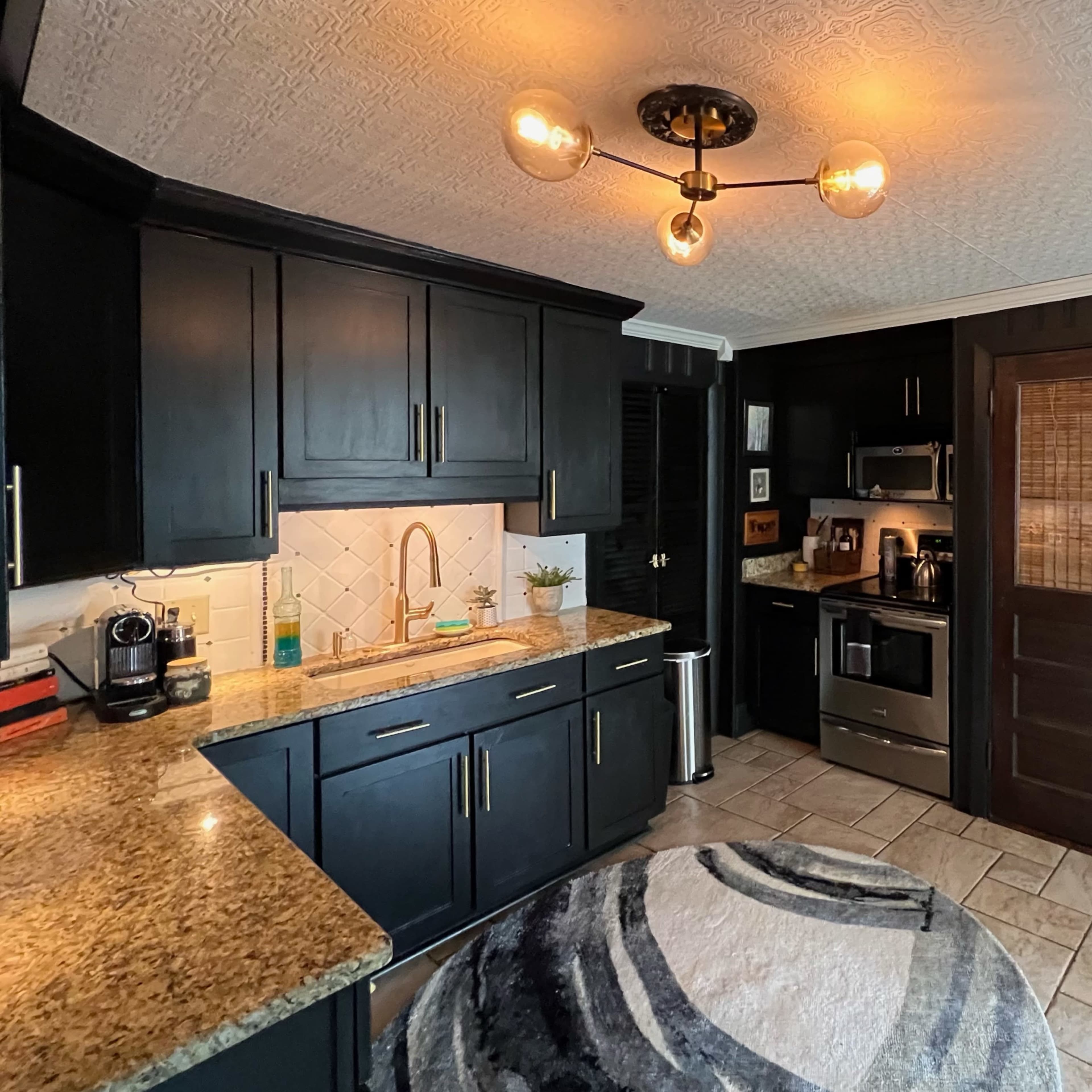 A modern kitchen features dark cabinetry, a stainless steel refrigerator, and a circular rug on tiled flooring.