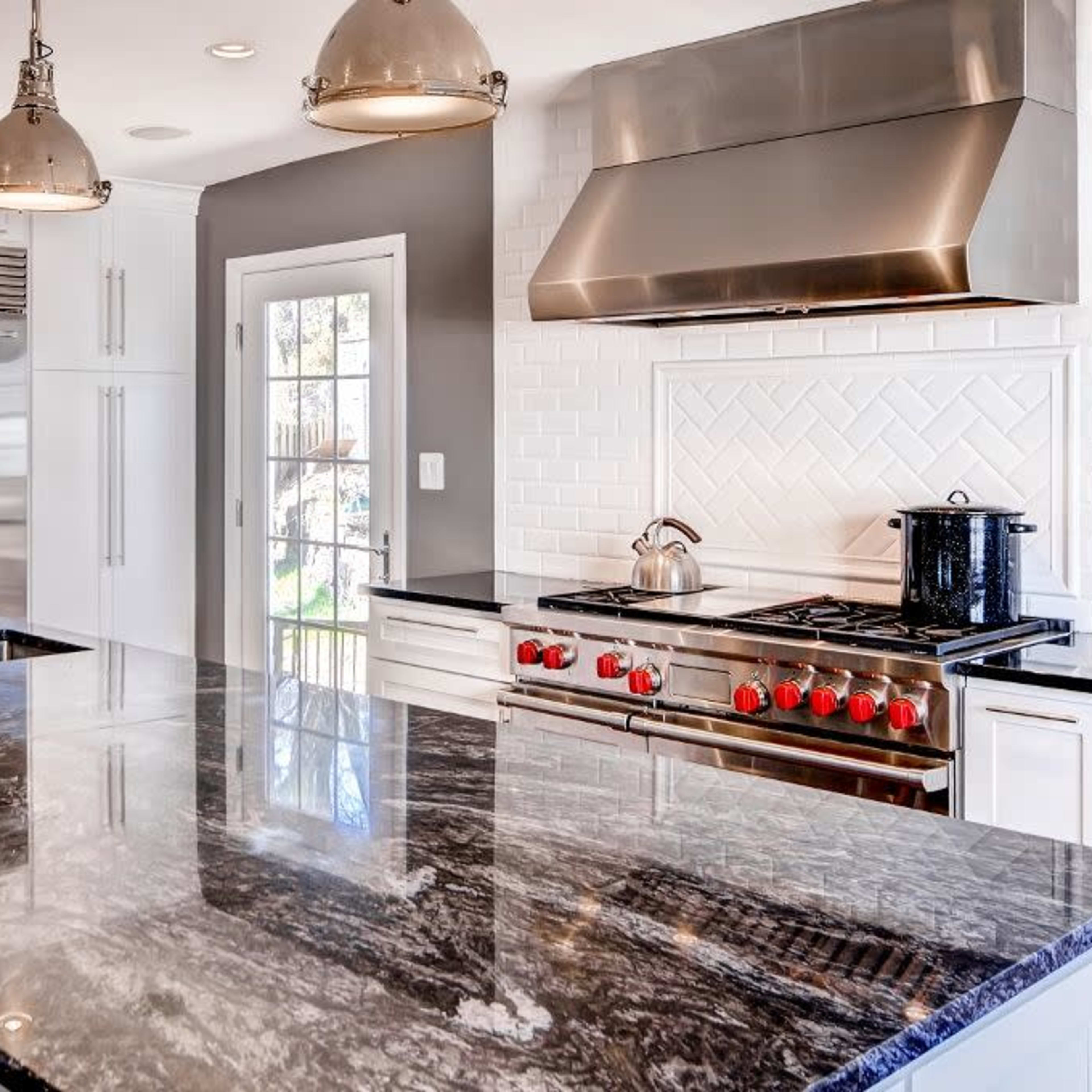 A modern kitchen featuring stainless steel appliances, a large granite island, and a gas stove with red knobs.