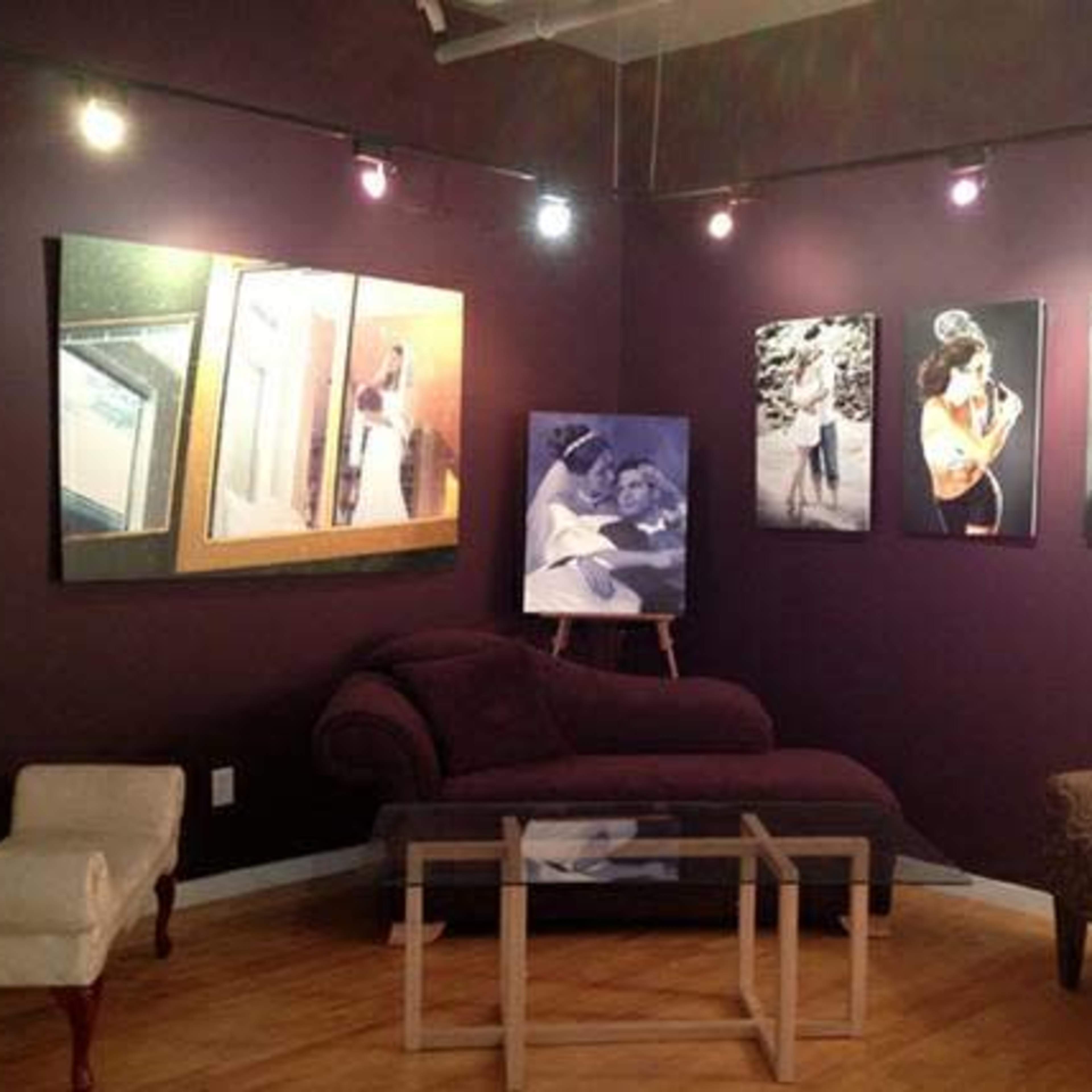 A small gallery with dark purple walls displaying various framed photographs, a chaise lounge, and seating arrangements around a glass coffee table.