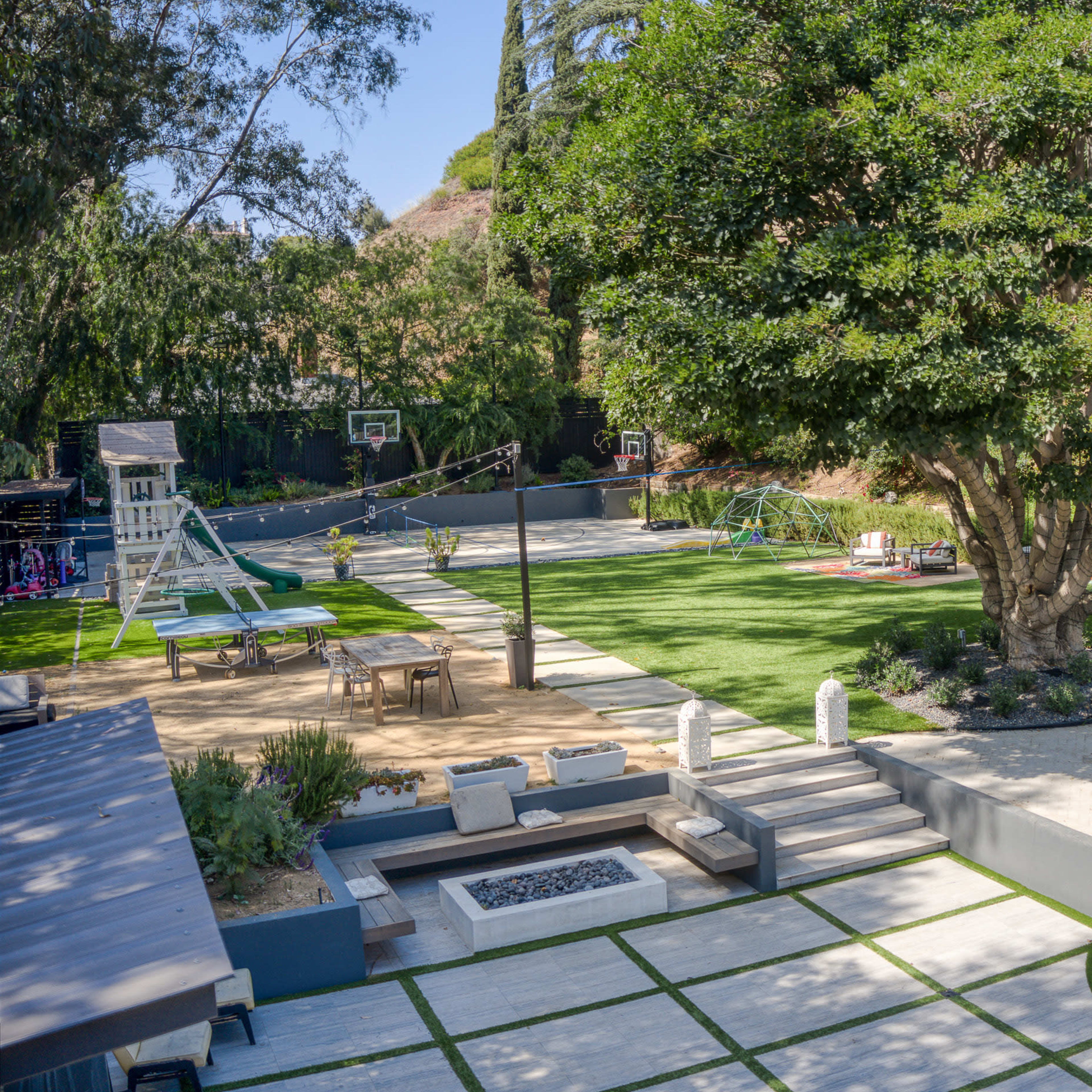A spacious backyard featuring a pool, seating area, playground equipment, and a large tree, with various recreational spaces and landscaping.
